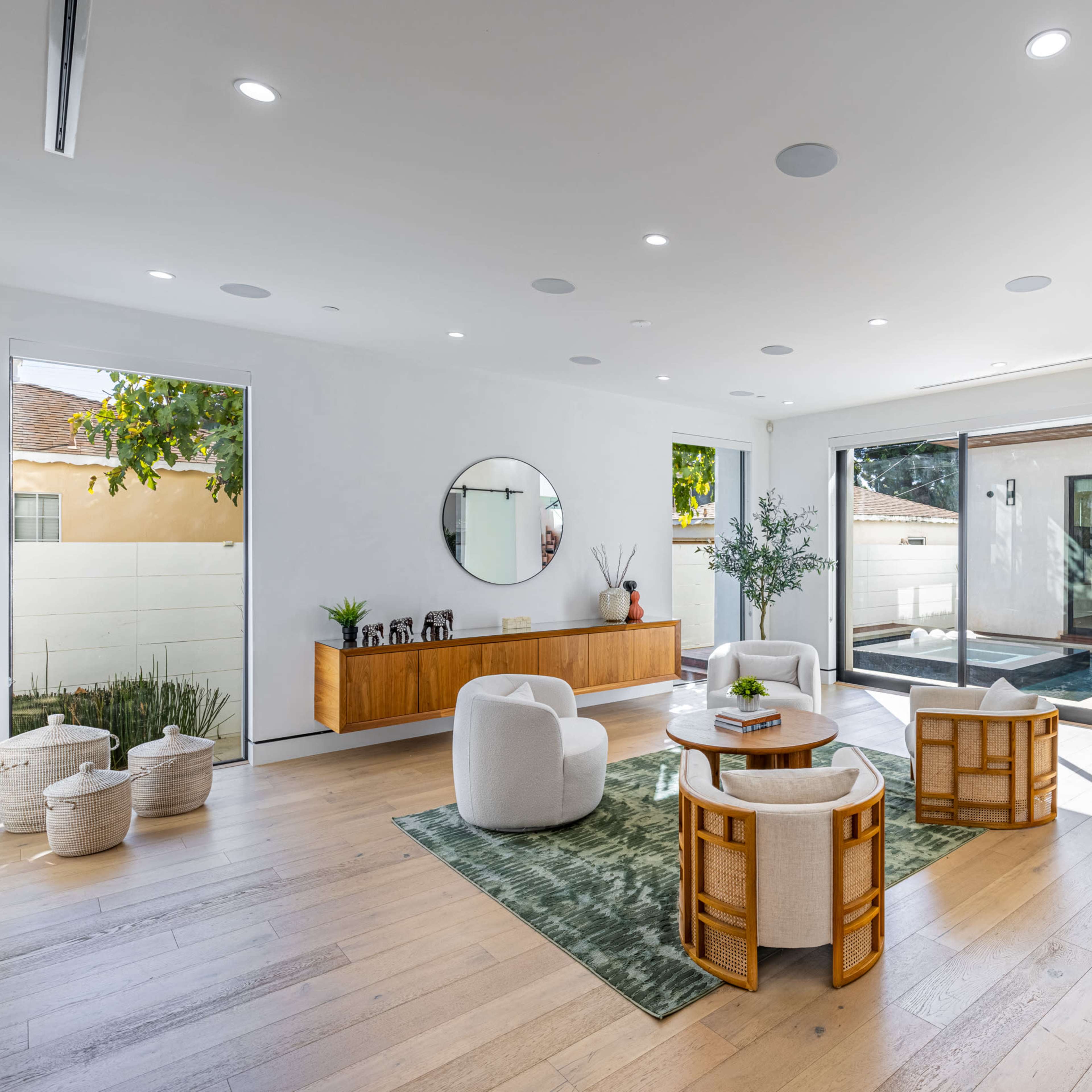 A spacious, modern living area featuring a round coffee table, four chairs, a large mirror on the wall, and glass doors leading to an outdoor space.