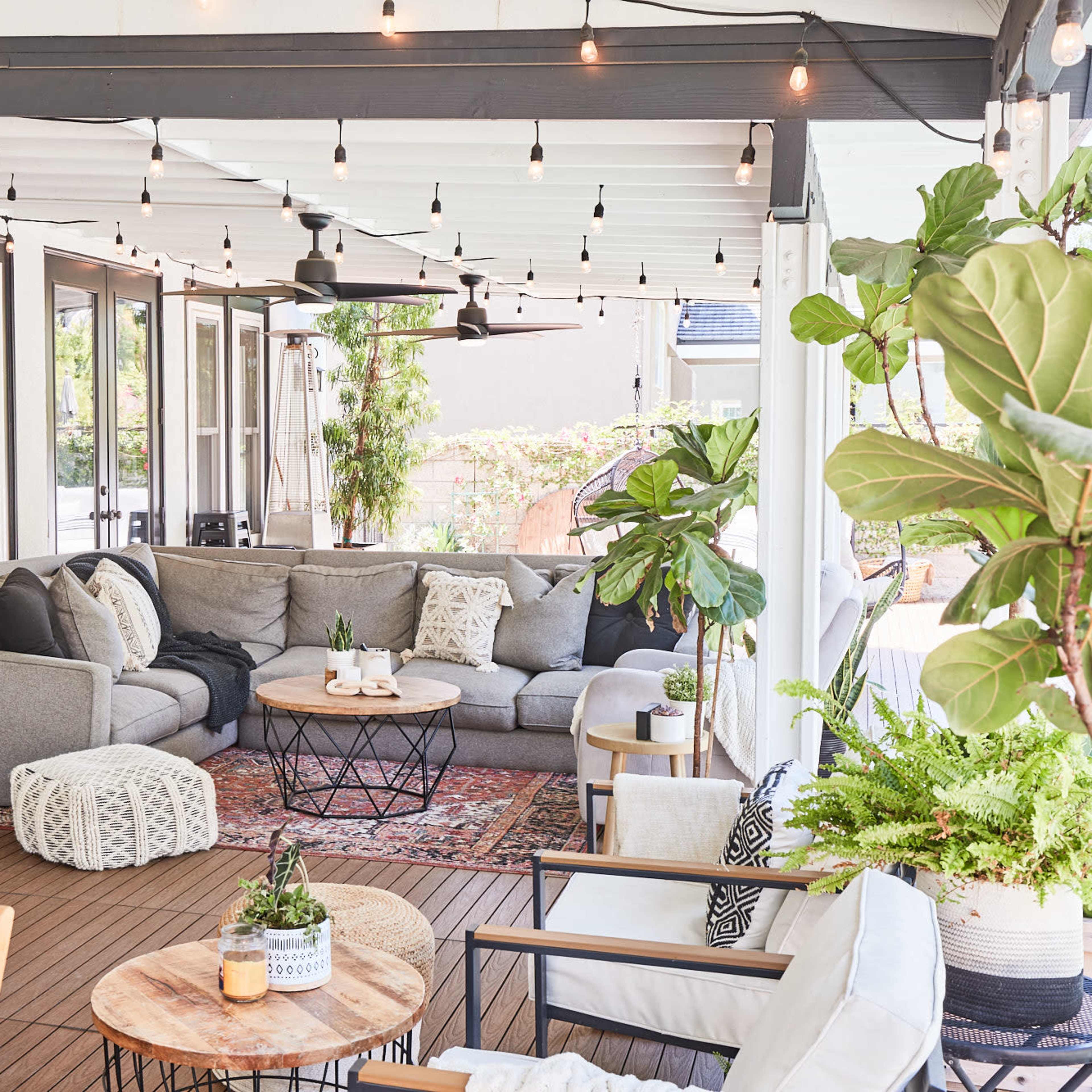 A spacious outdoor patio features a gray sectional sofa, a round coffee table, potted plants, and string lights overhead.
