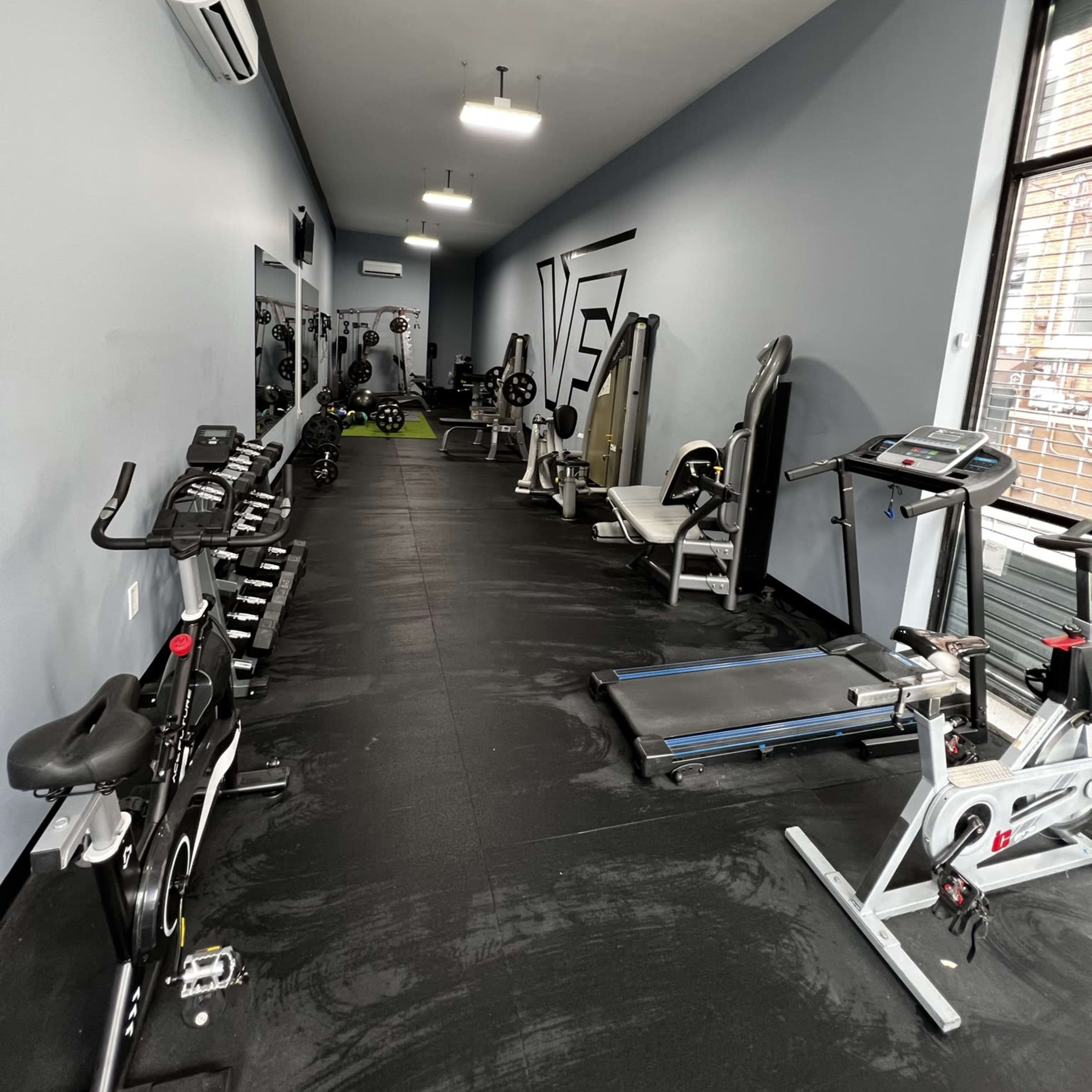 A narrow gym space equipped with various exercise machines and weights along the walls.