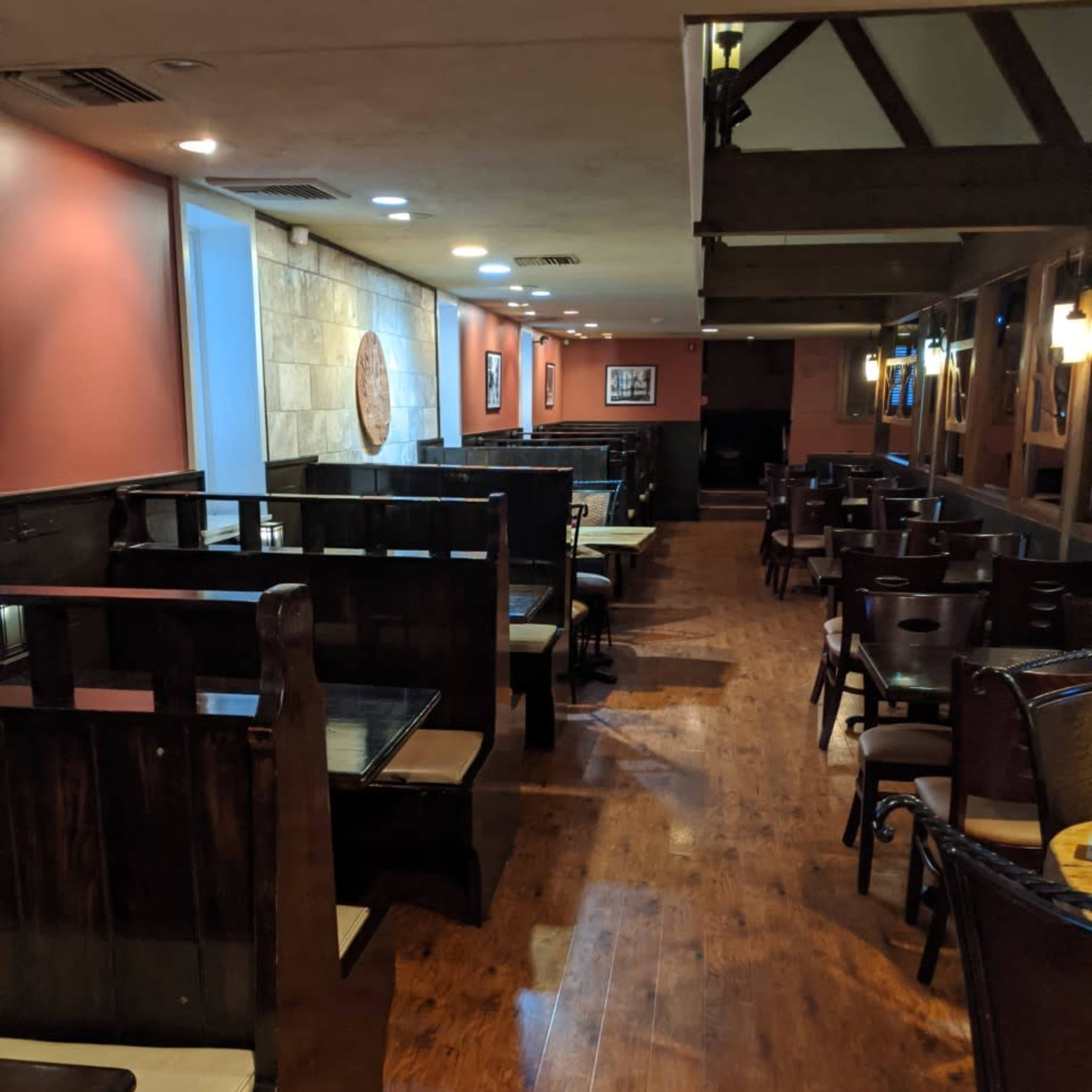 A restaurant interior featuring wooden booths along the walls and empty tables arranged throughout the space.