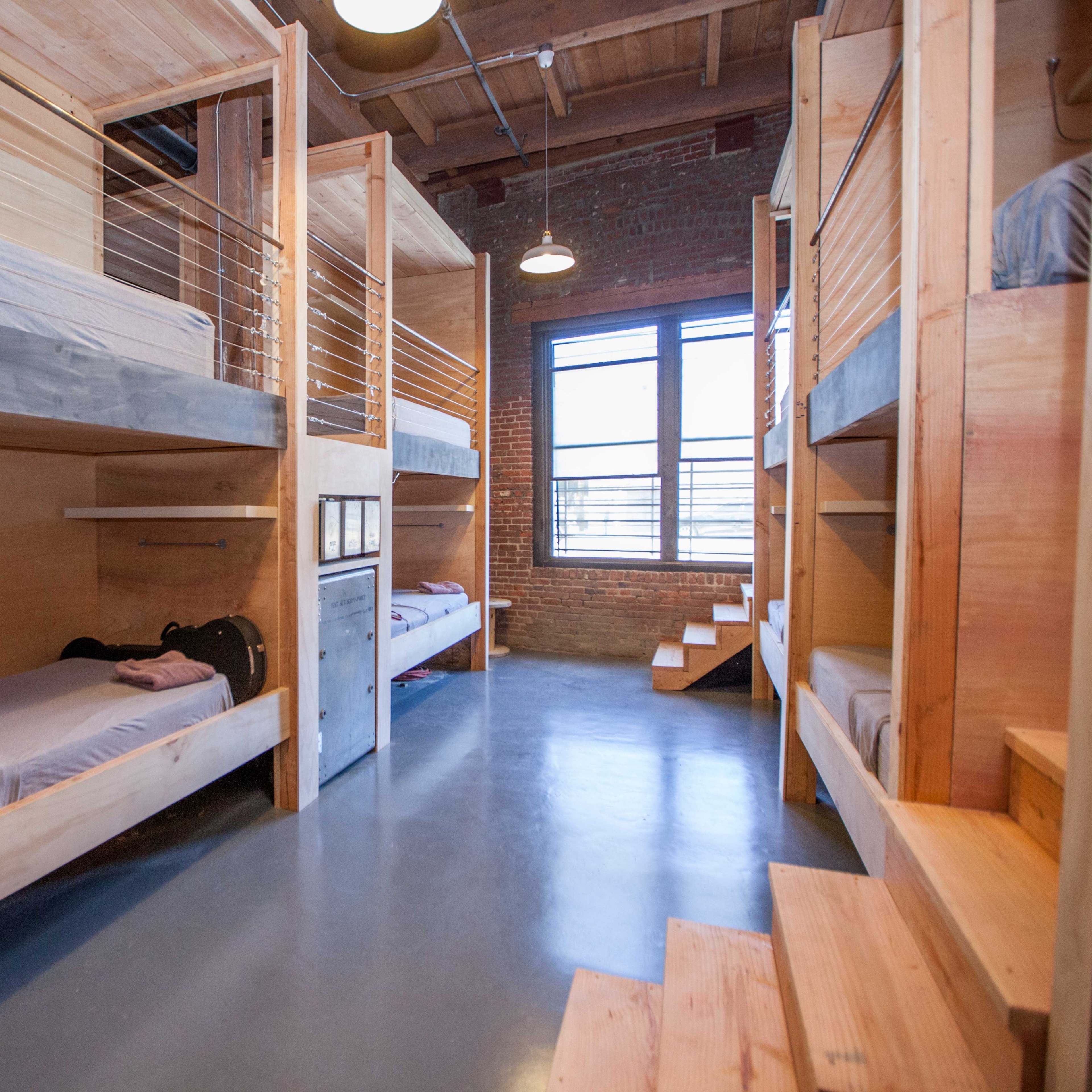 A modern bunk room with wooden bunk beds and a large window allowing natural light to enter.