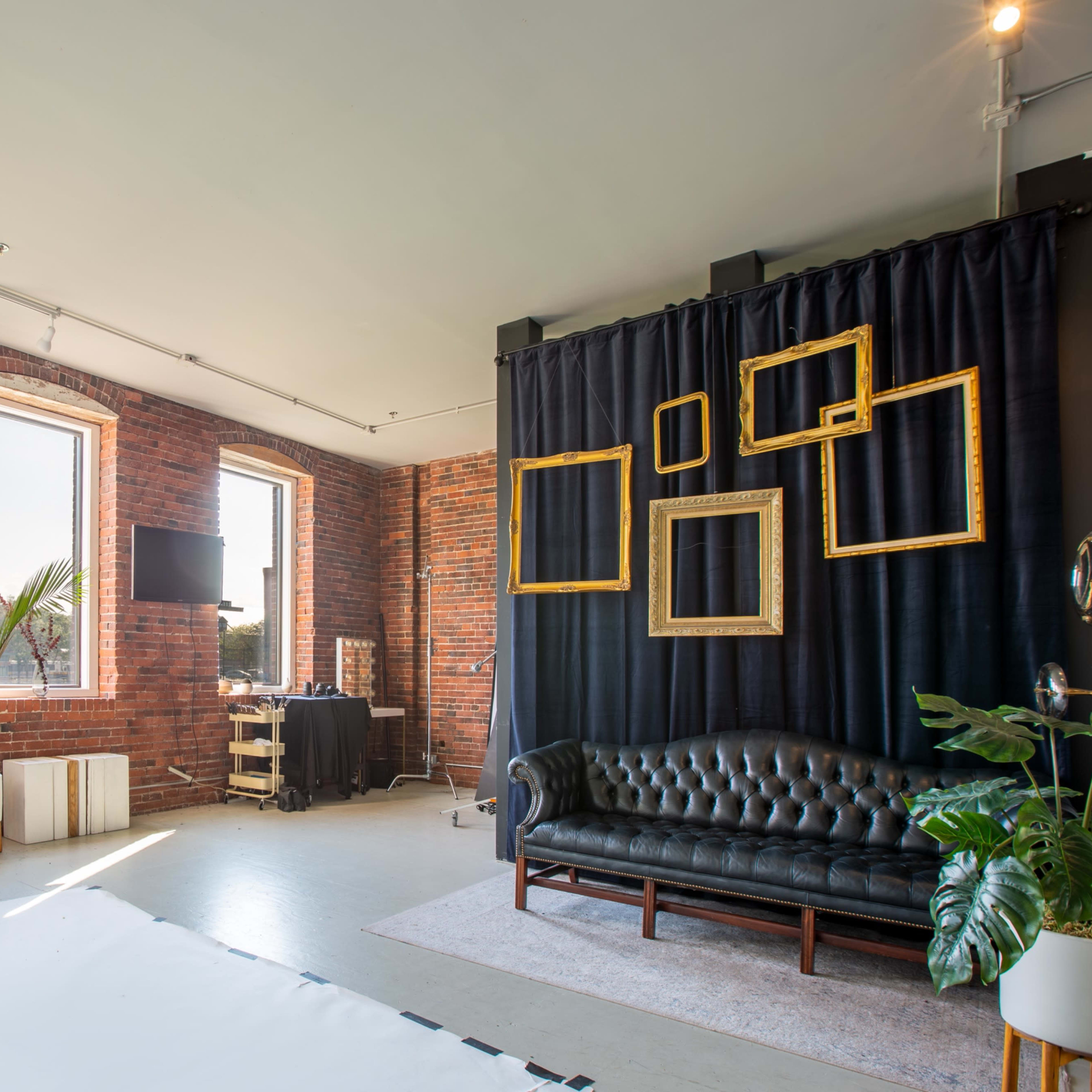 A modern interior with exposed brick walls, large windows, a leather sofa, and a dark curtain featuring empty picture frames.