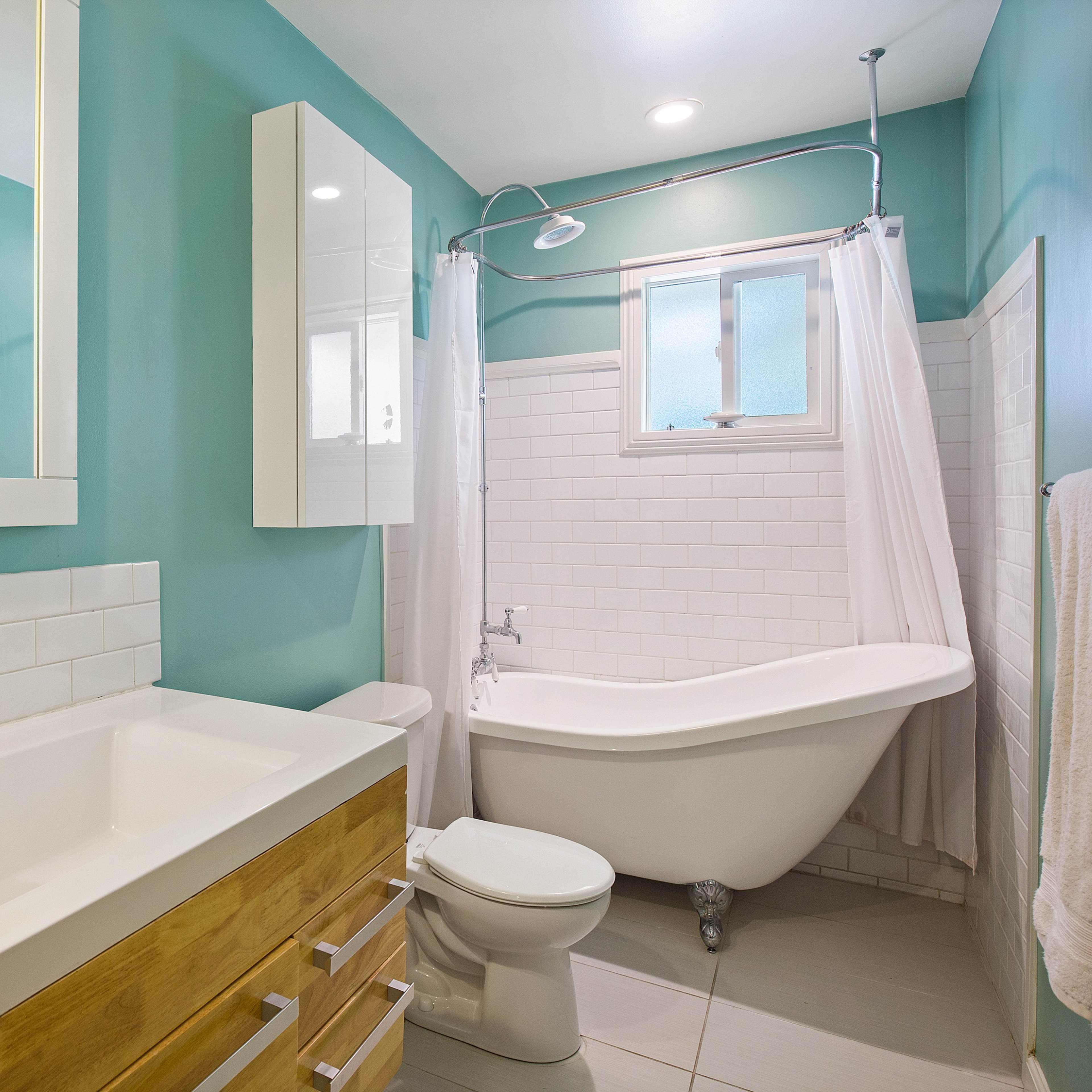 The bathroom features a freestanding tub, a shower with a glass enclosure, a wooden vanity with a sink, and light turquoise walls.