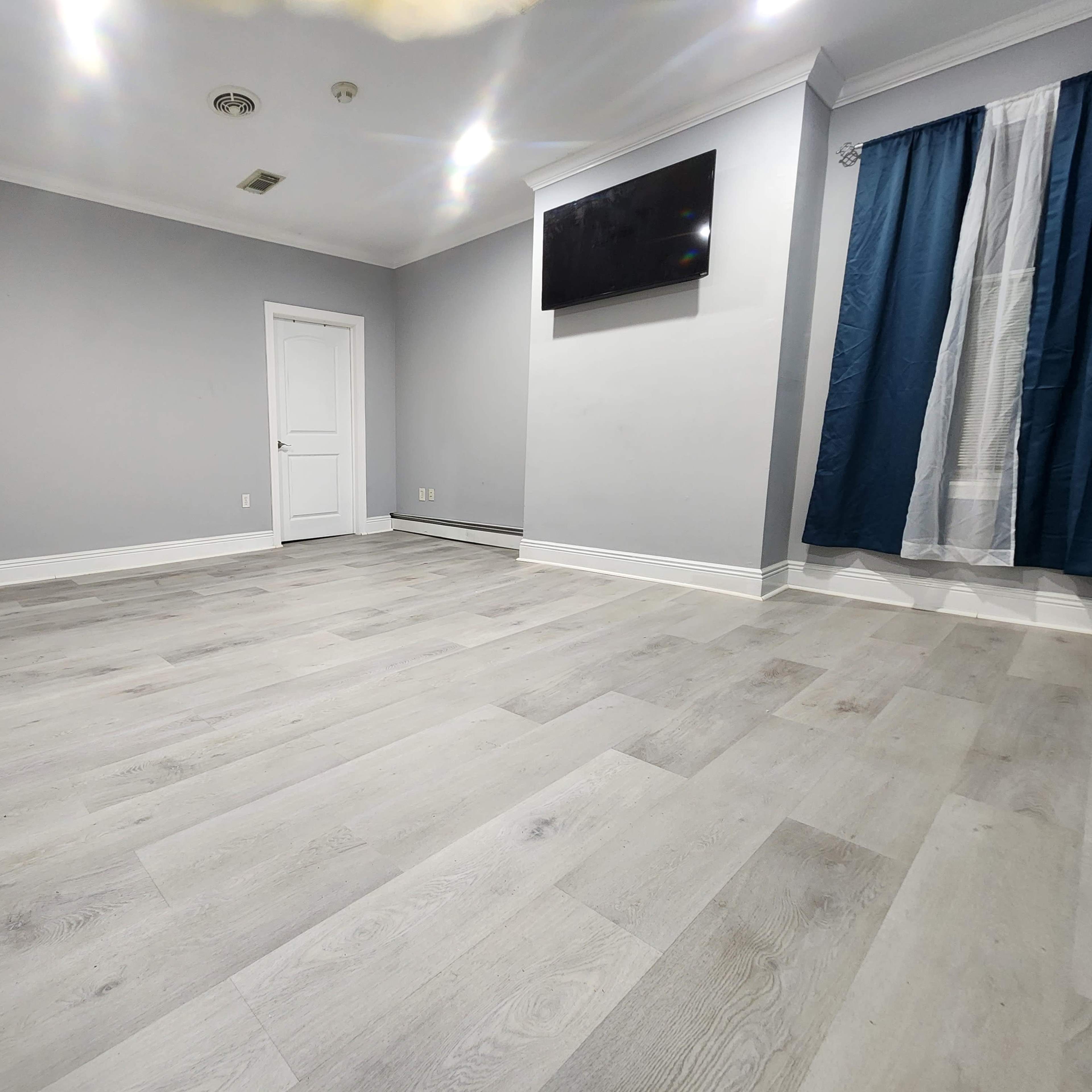 A sparse room with light gray walls, a TV mounted on one wall, and light wood flooring.