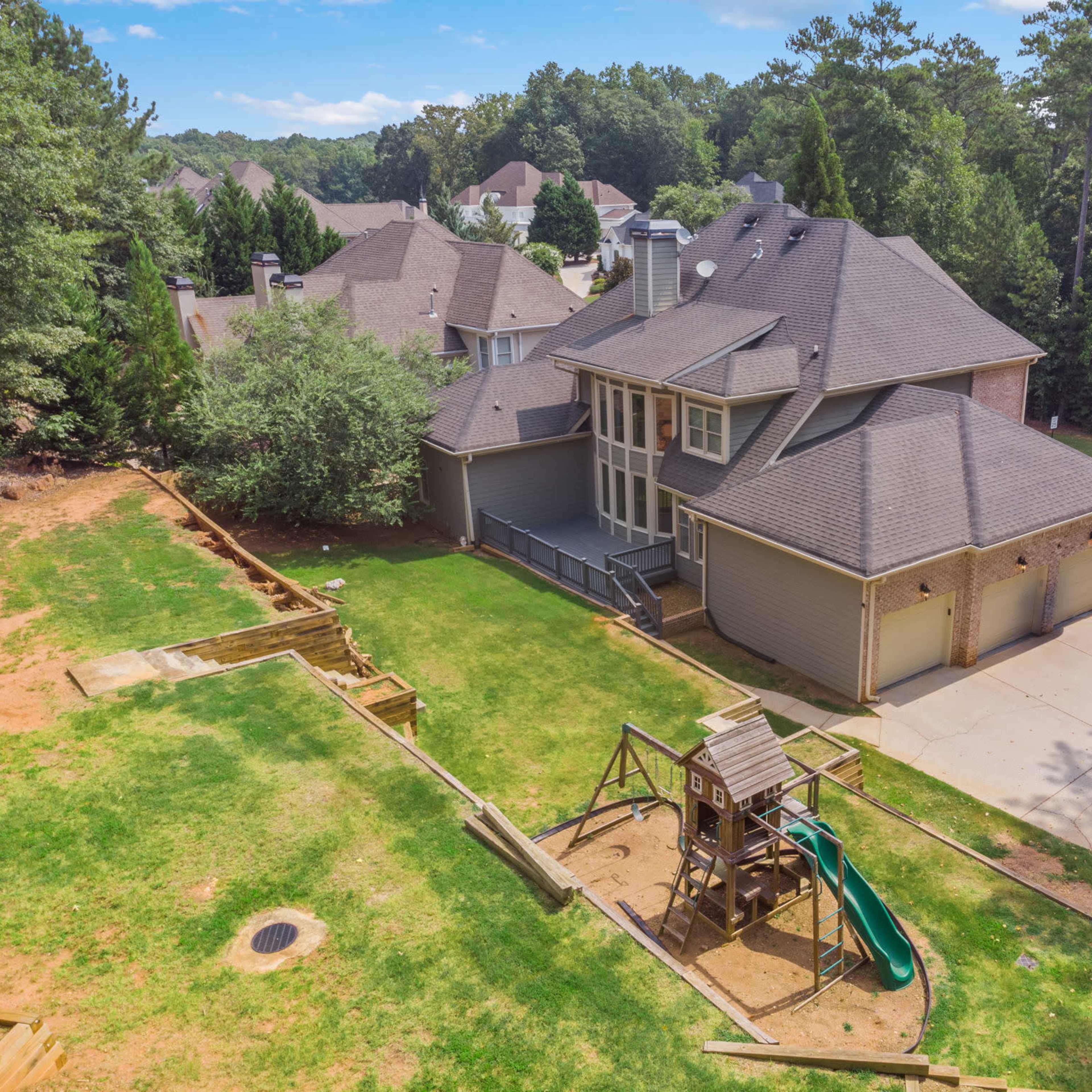 Aerial view of a two-story house with a large backyard featuring a wooden playset and surrounding trees.