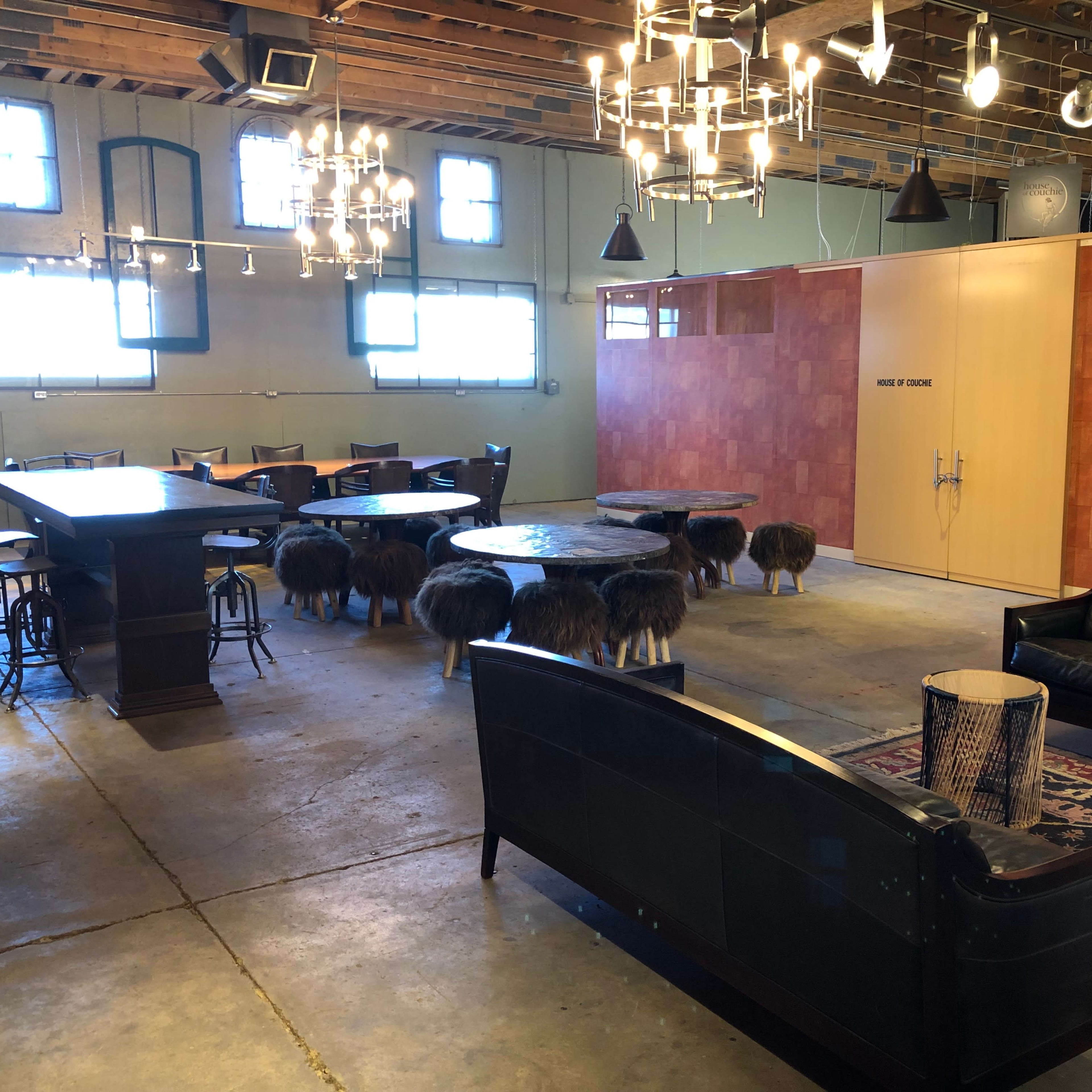 A spacious room with a large wooden table, various seating areas, and several animal-shaped stools arranged on a concrete floor.