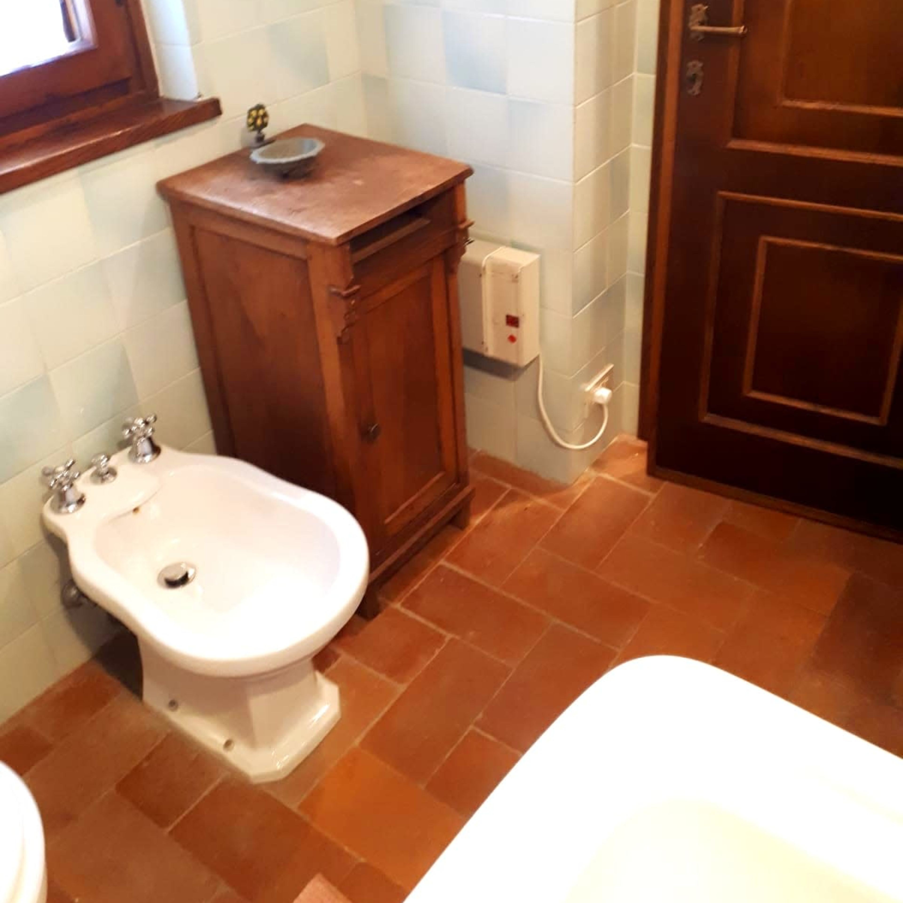 A bathroom featuring a bidet, a wooden cabinet, and a doorway.