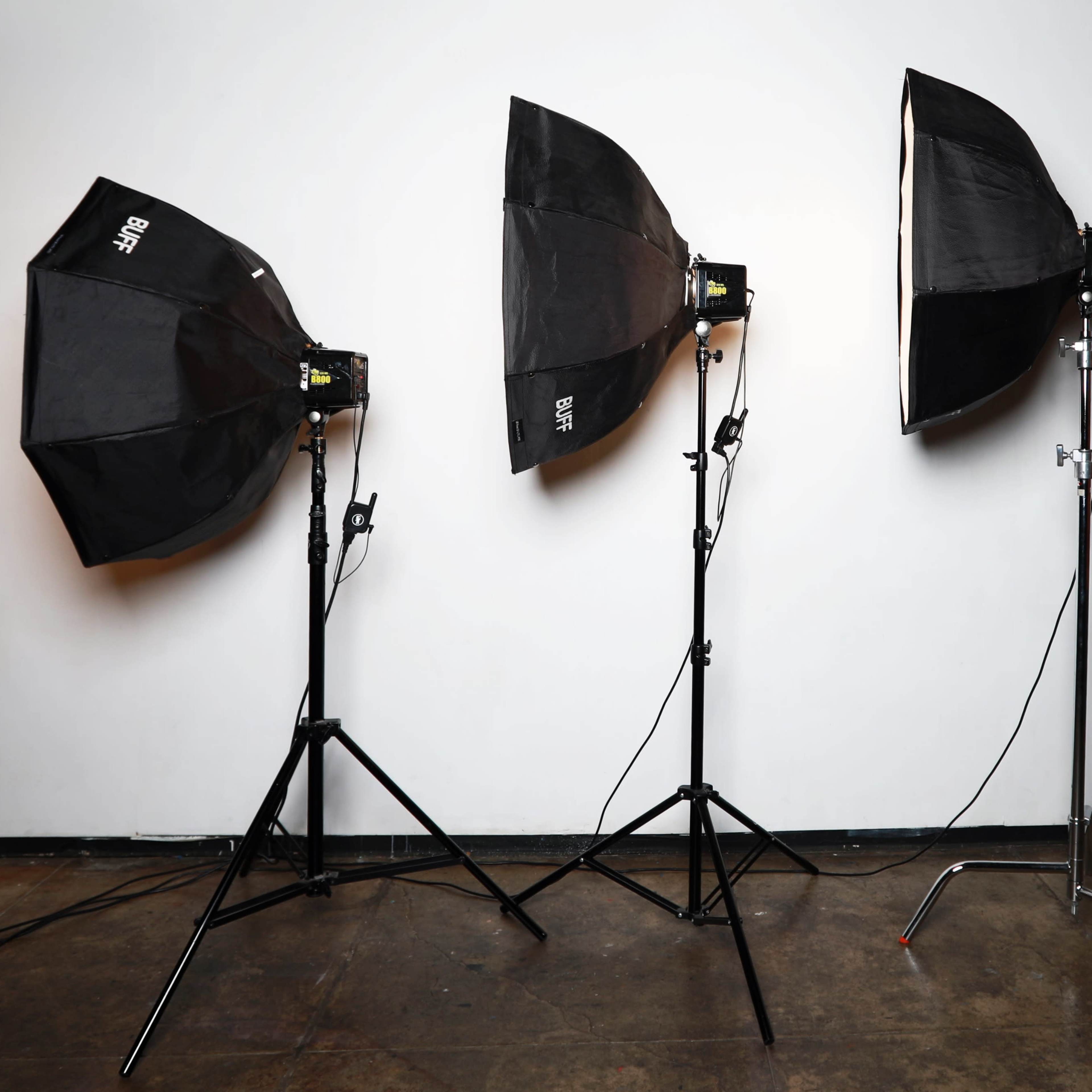 Three lighting softboxes on stands, positioned in front of a plain white backdrop.