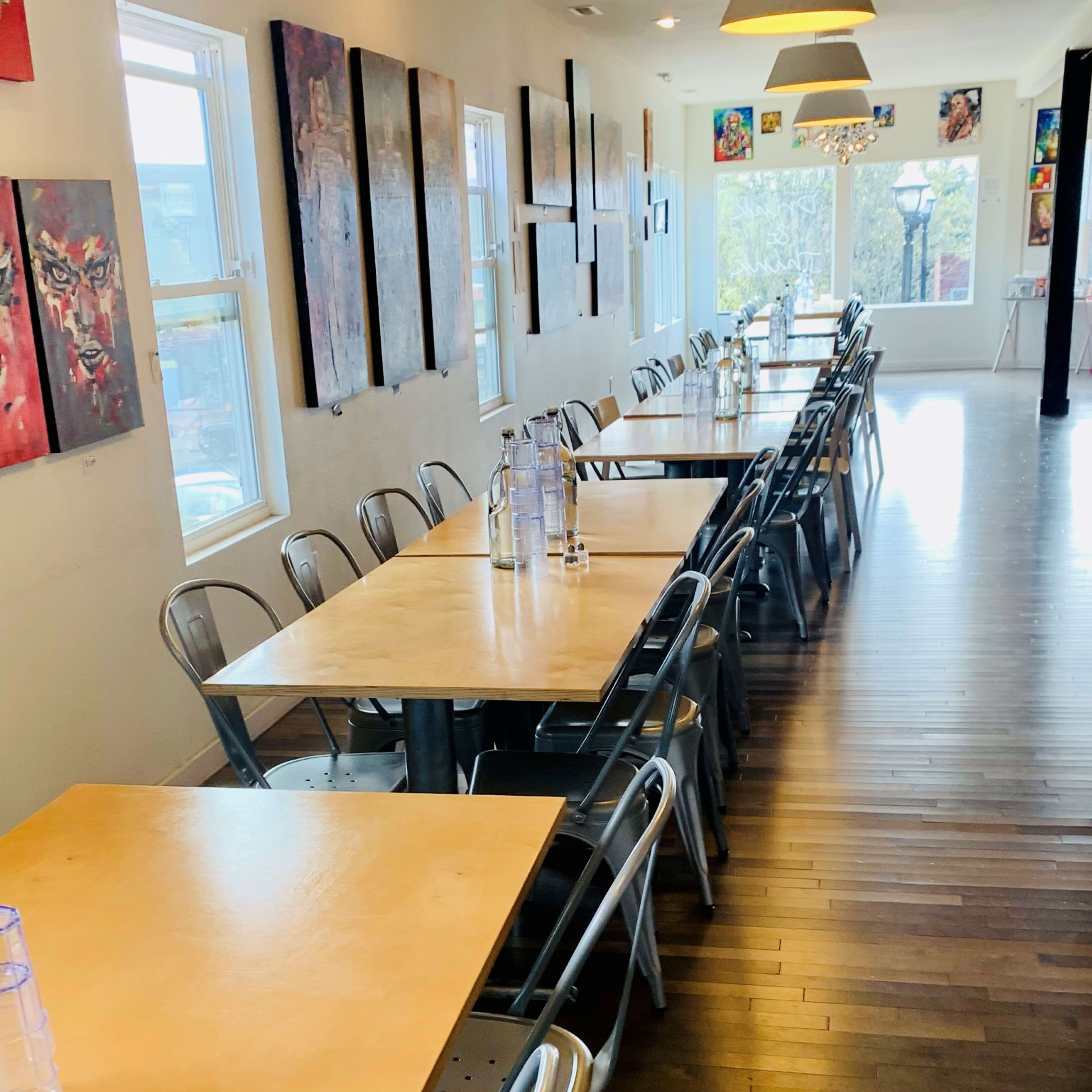 A spacious dining area features wooden tables and metal chairs, lined with colorful artwork on the walls.