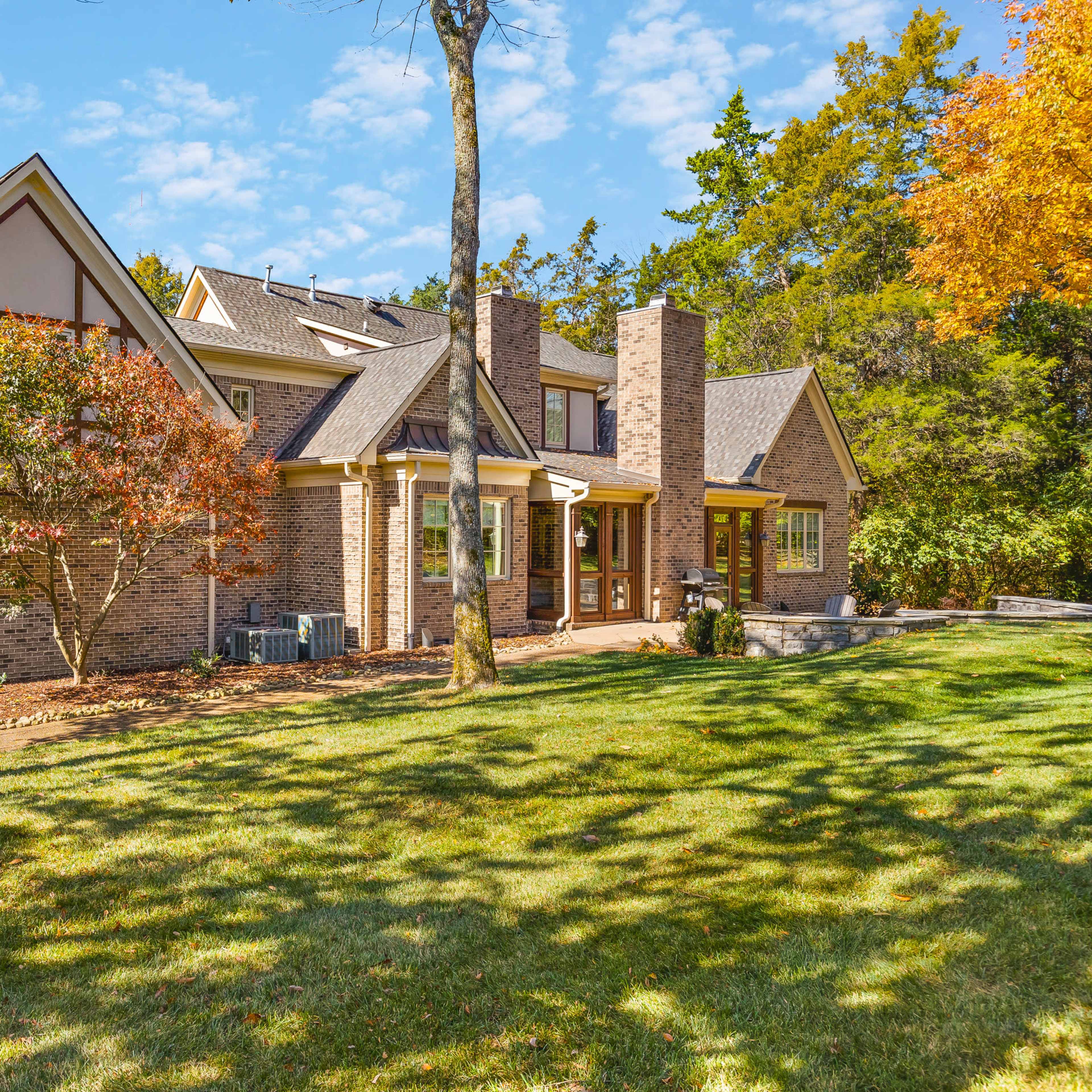A large brick house with a mix of architectural styles is surrounded by trees and a manicured lawn.
