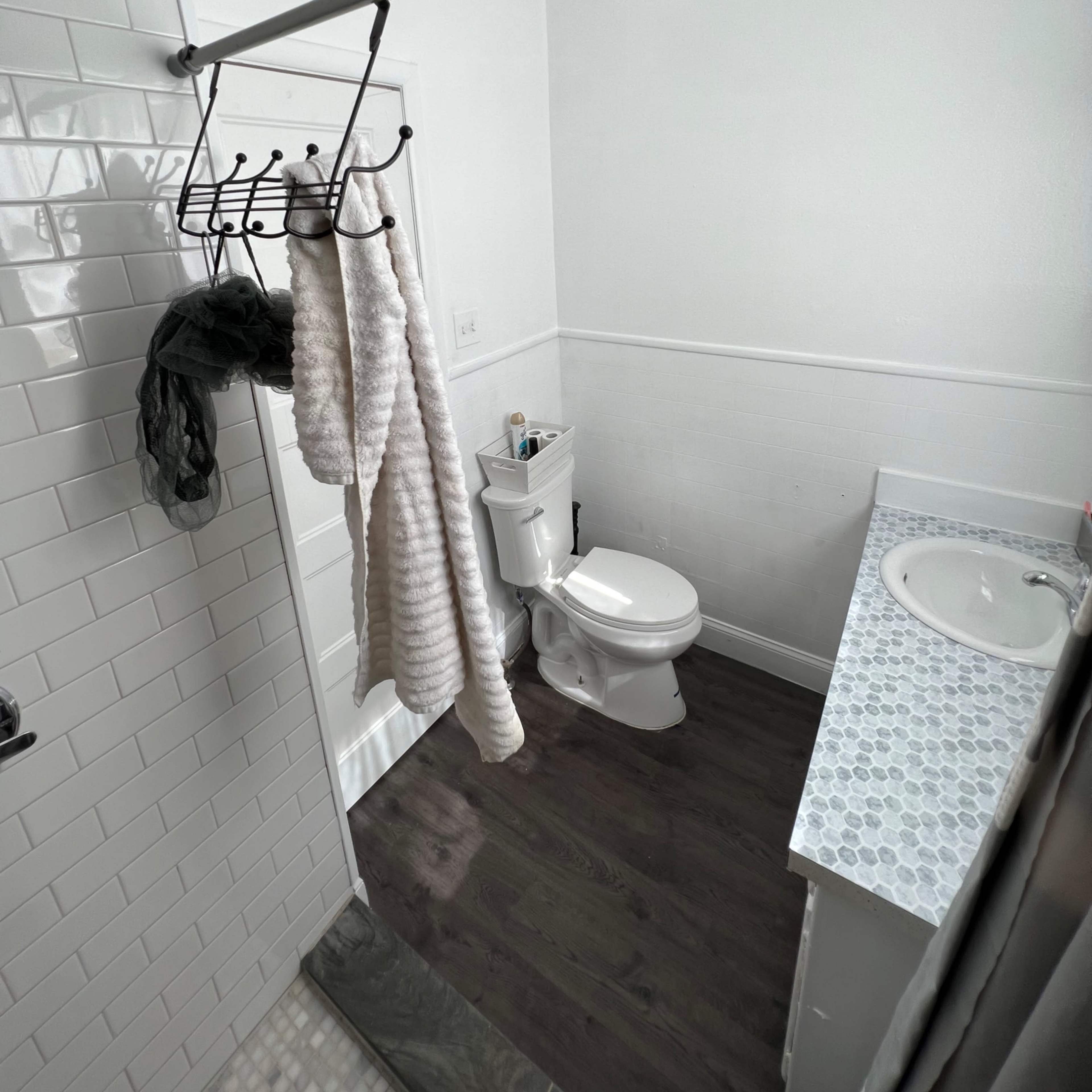 A bathroom with a shower area, a toilet, and a sink on a counter, featuring a towel rack with hanging towels.