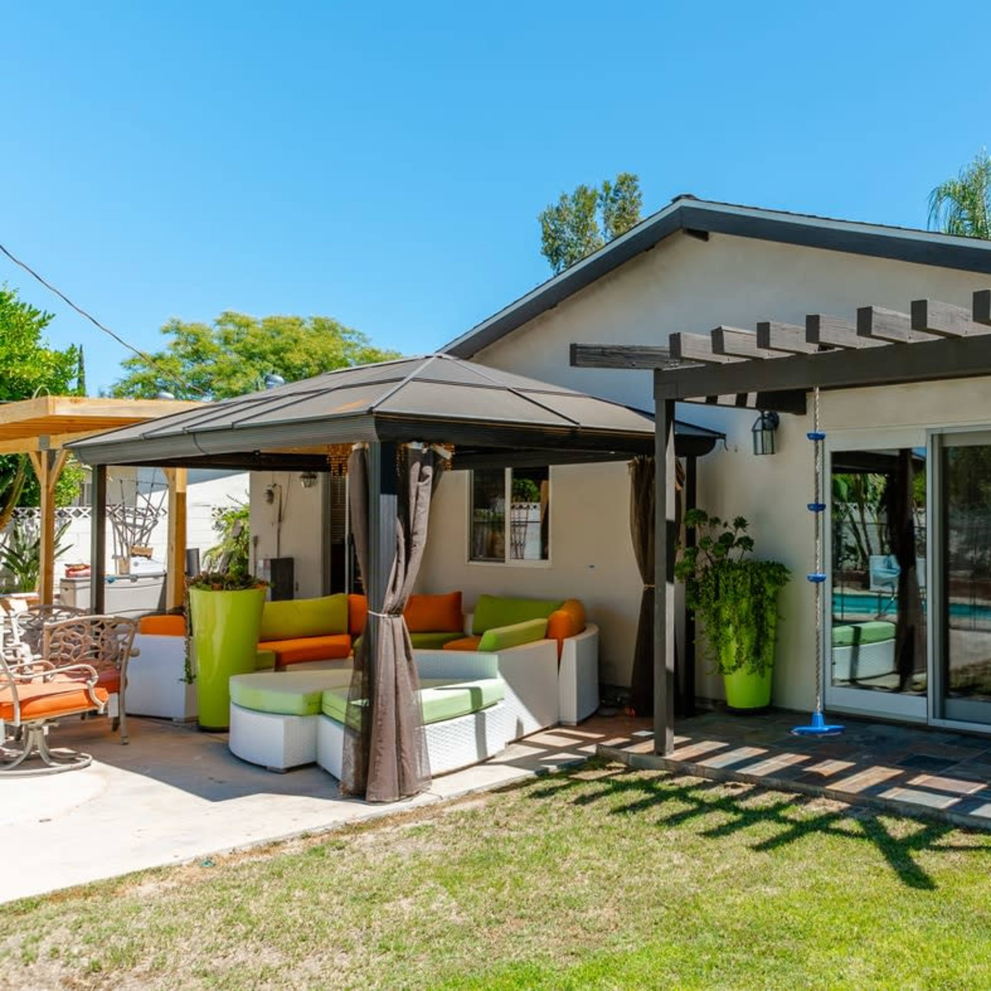 A modern backyard features a patio area with a gazebo and a seating arrangement next to a house.