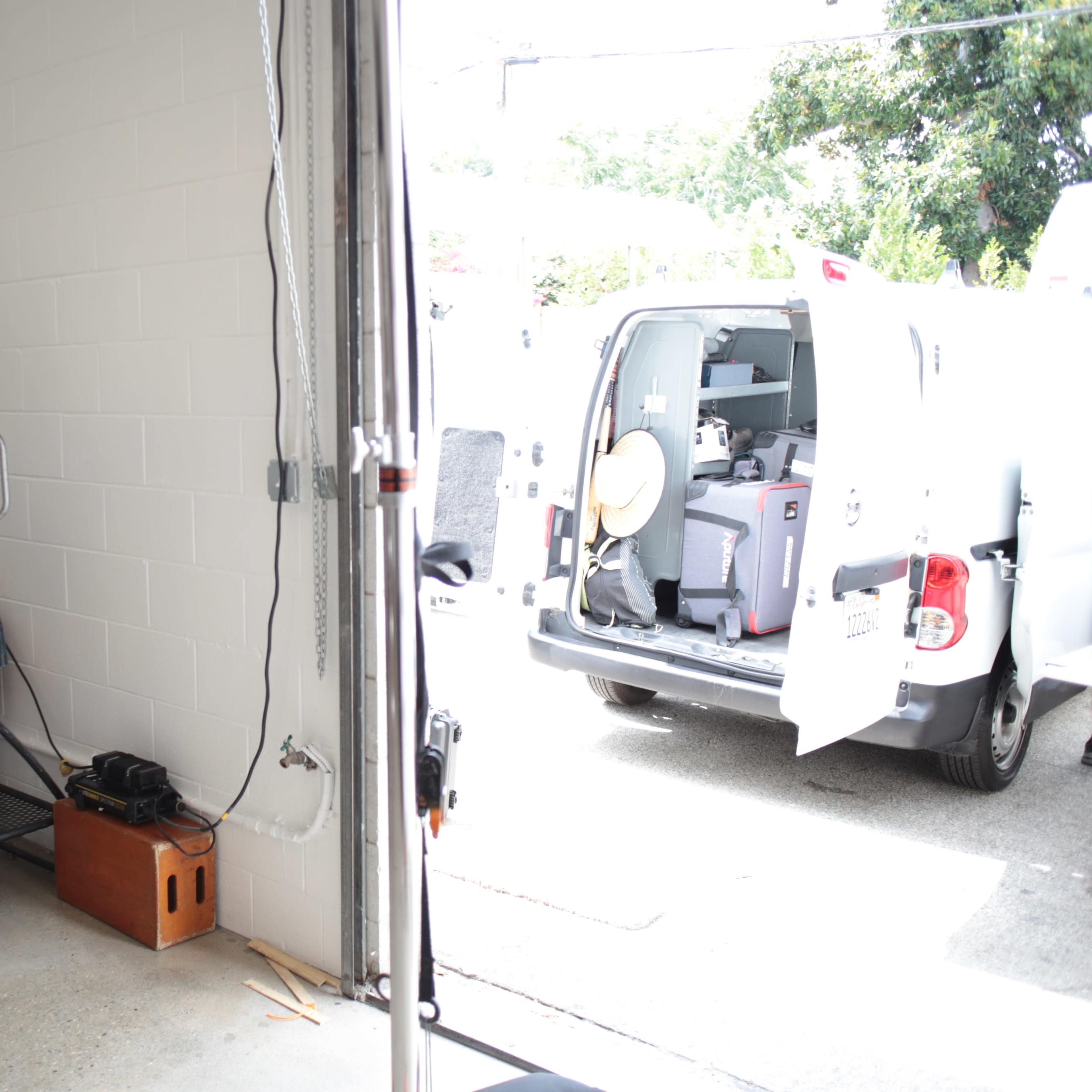 A garage with equipment and tools on the left and an open van loaded with supplies on the right.