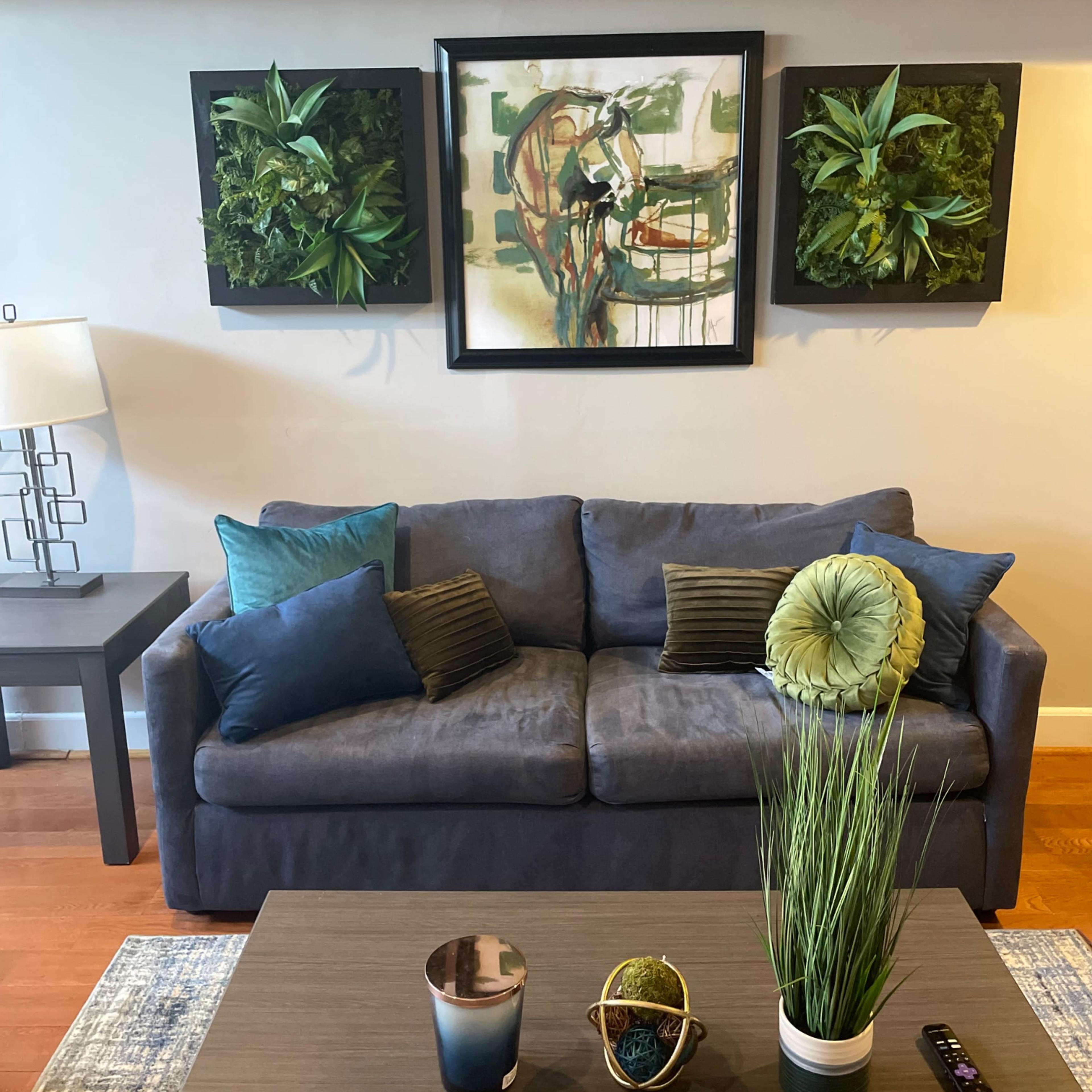 A living room with a gray couch, a coffee table adorned with decorative plants, and wall art featuring greenery.