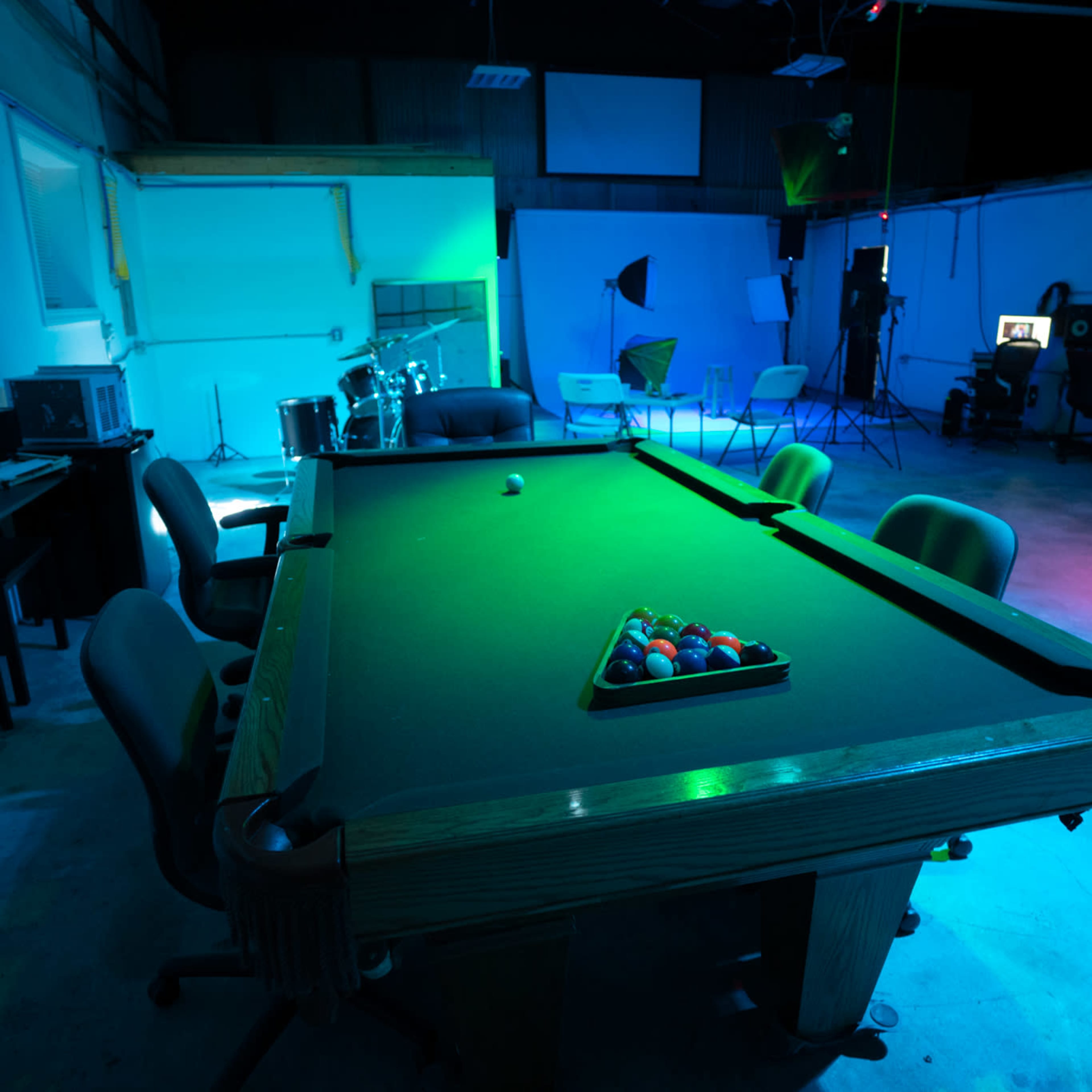 A billiard table with a full set of colored balls is positioned in a dimly lit room featuring studio equipment and seating areas.