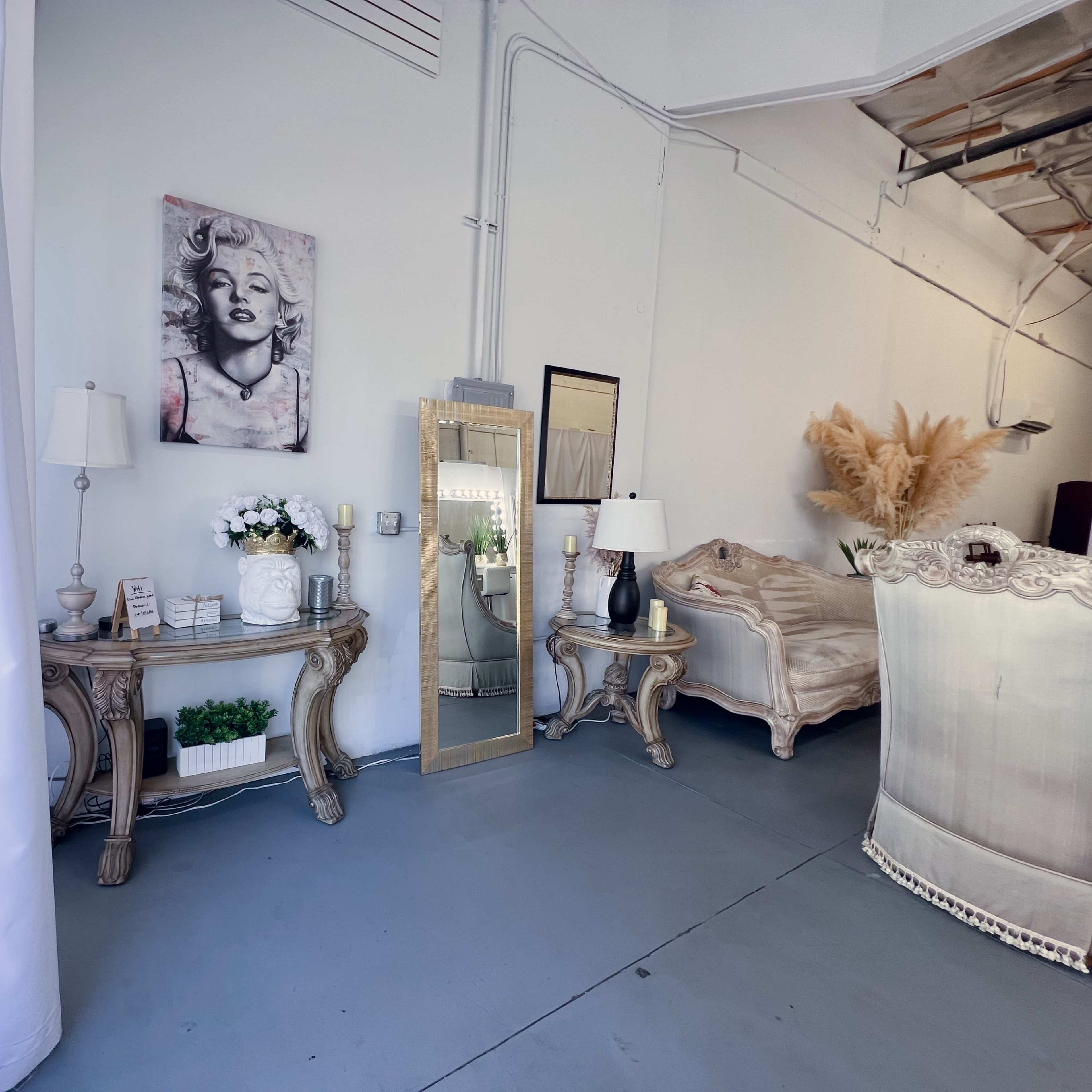 A stylish interior featuring a large mirror, decorative lamps, a bed, and a framed artwork of a woman on the wall.