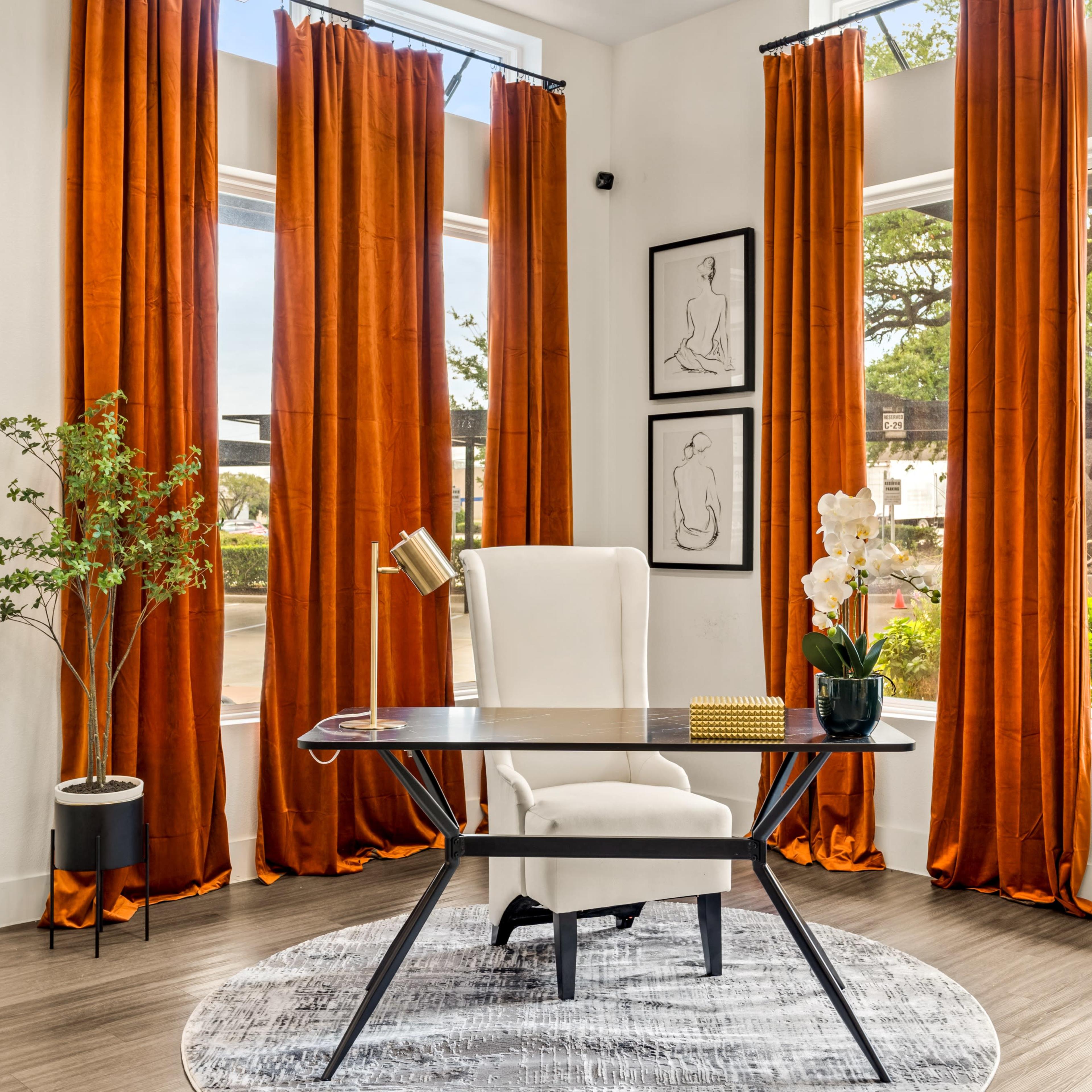 A stylish office space featuring a white chair, a glass desk with a lamp, and orange curtains framing large windows overlooking greenery.