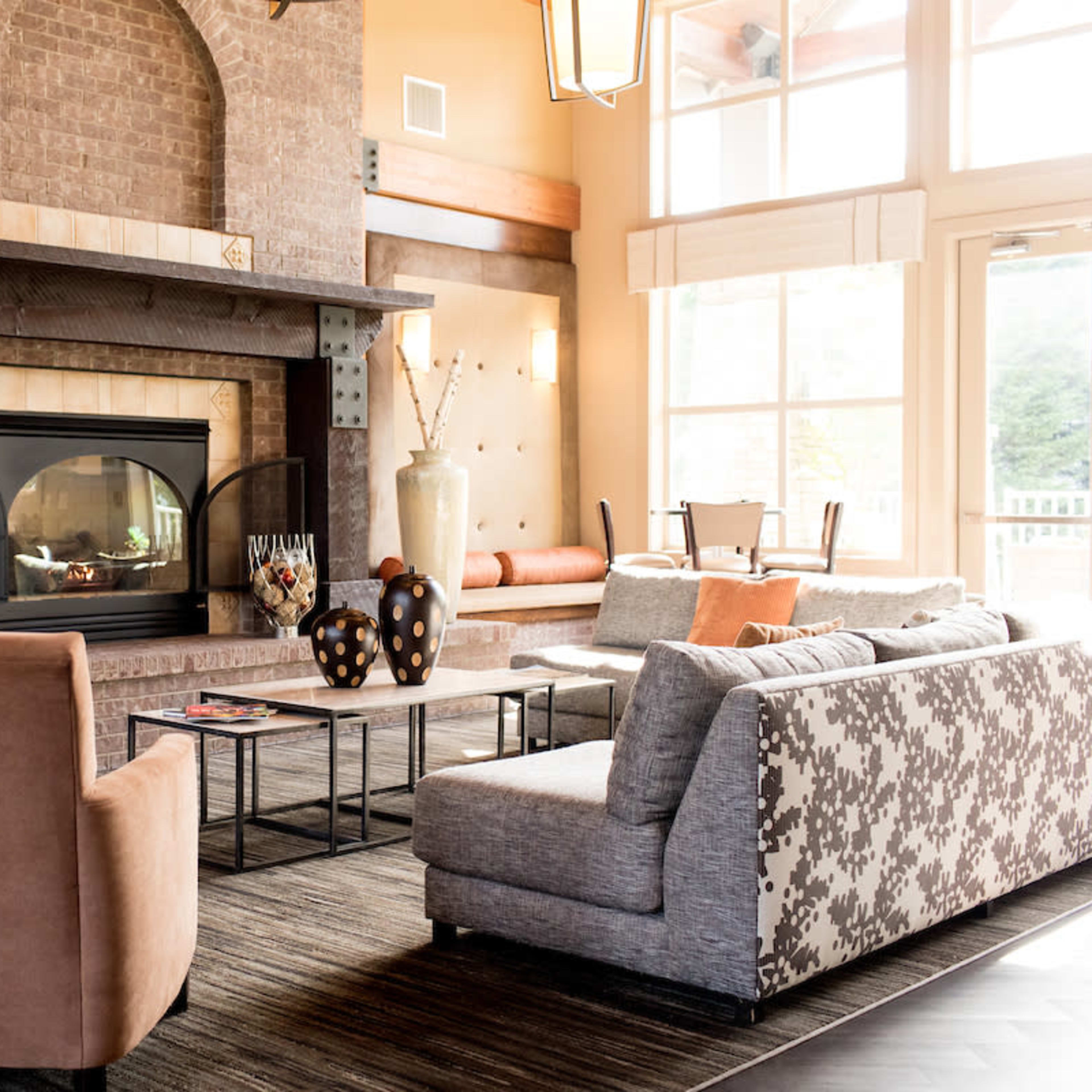 A cozy living room featuring a large fireplace, comfortable seating arrangements, and large windows allowing natural light to enter the space.