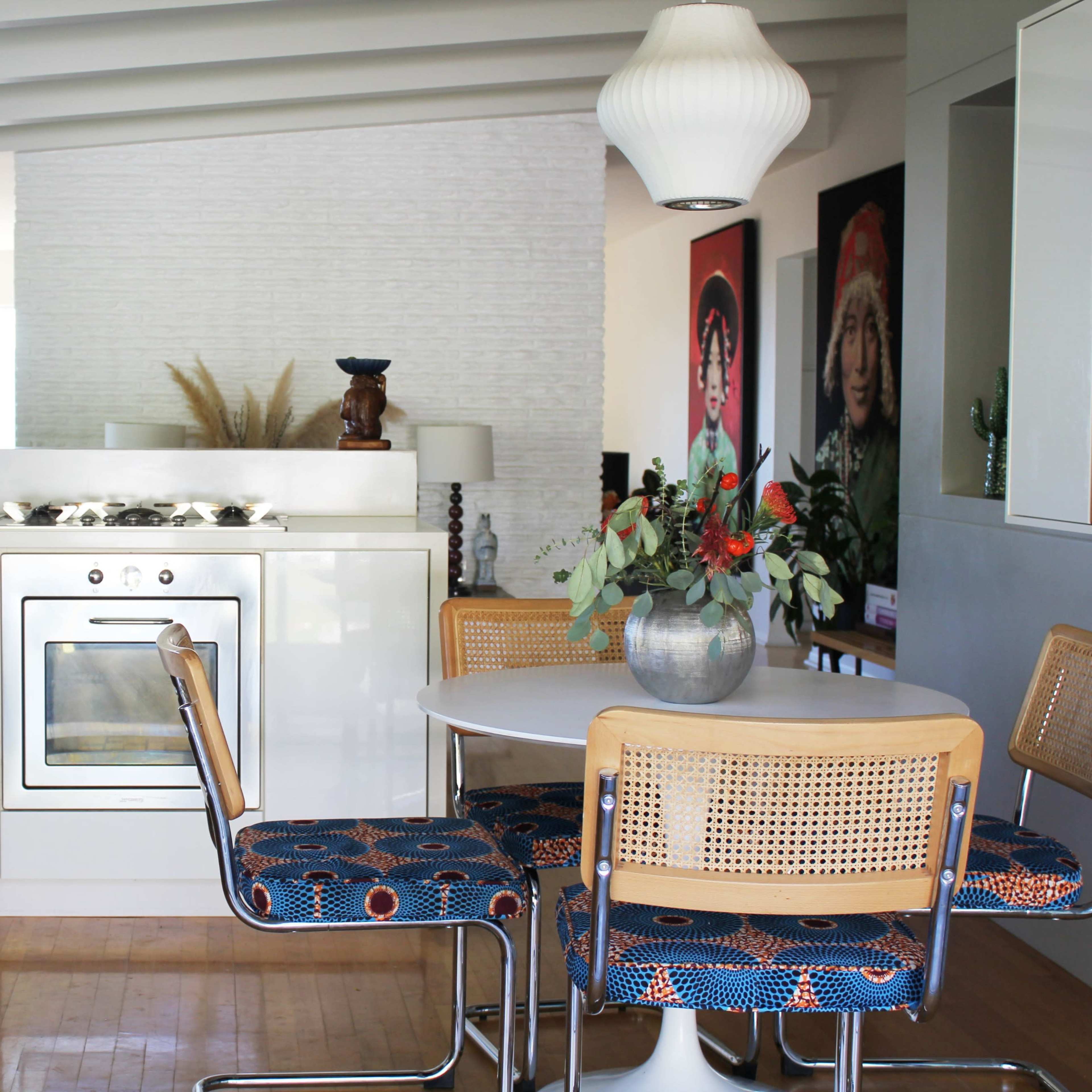 A modern kitchen and dining area featuring a round table with rattan chairs, an oven integrated into a white cabinetry, and decorative plants on the table and countertops.