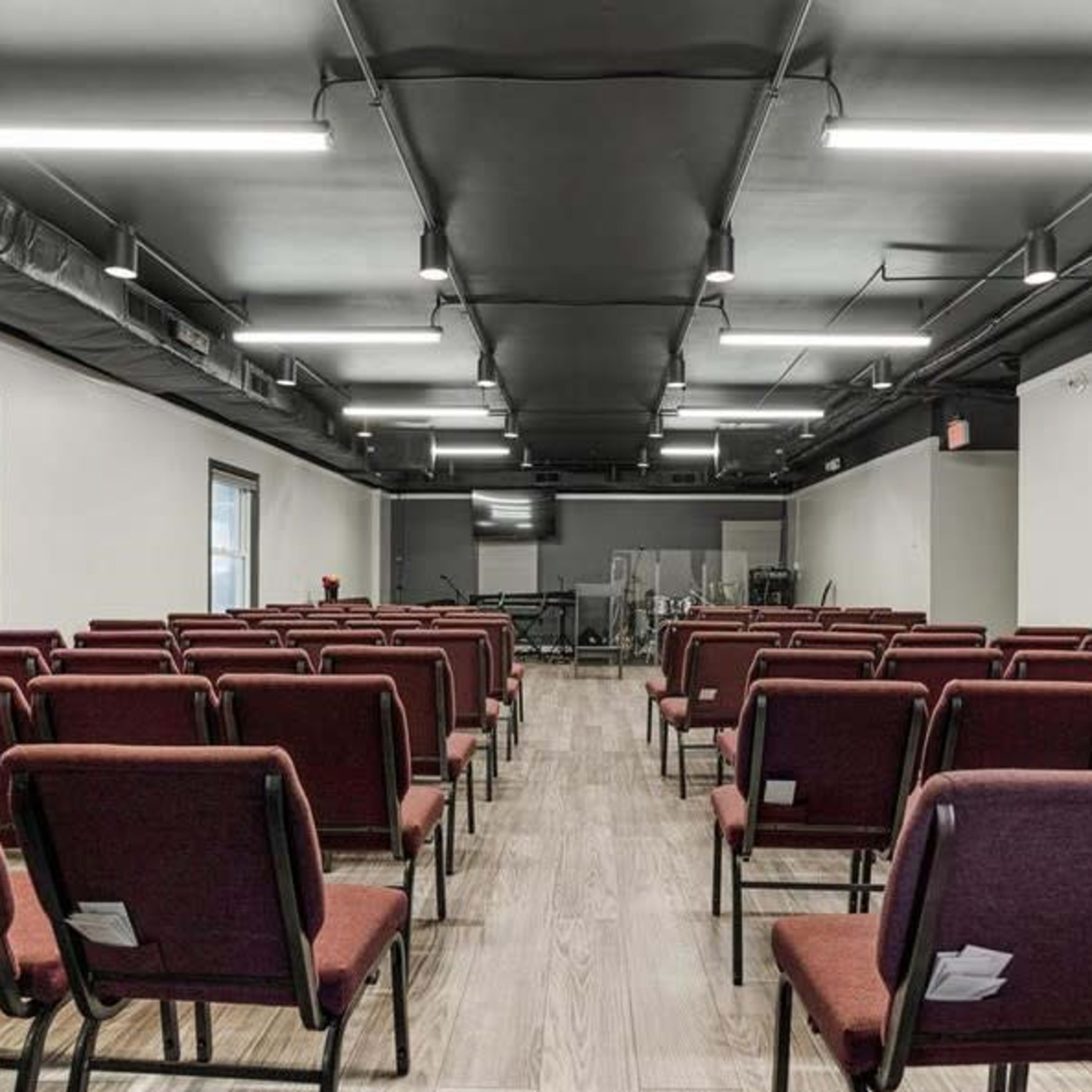 An interior space arranged with red chairs facing a stage area, illuminated by overhead lighting.