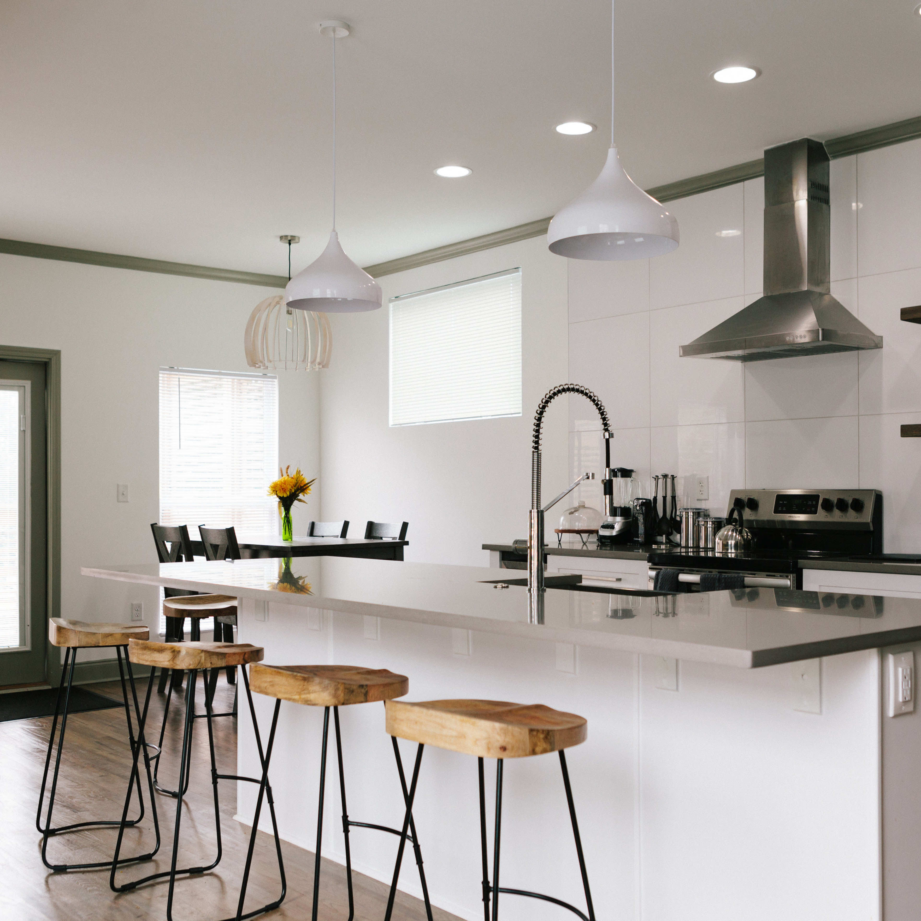 A modern kitchen features sleek white cabinetry, stainless steel appliances, and a large island with wooden stools.