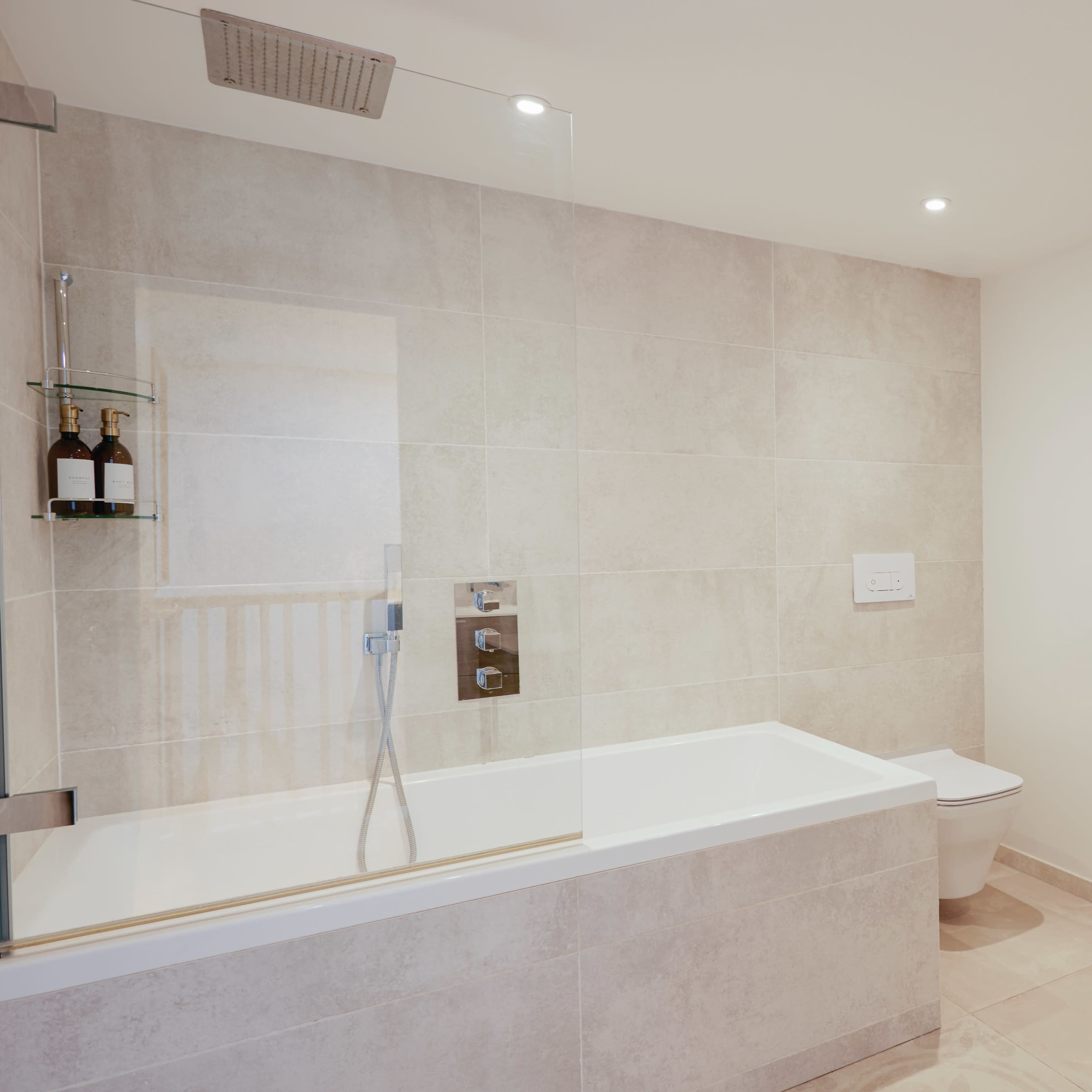 A modern bathroom featuring a bath with a glass shower enclosure, a wall-mounted toilet, and a heated towel rail.