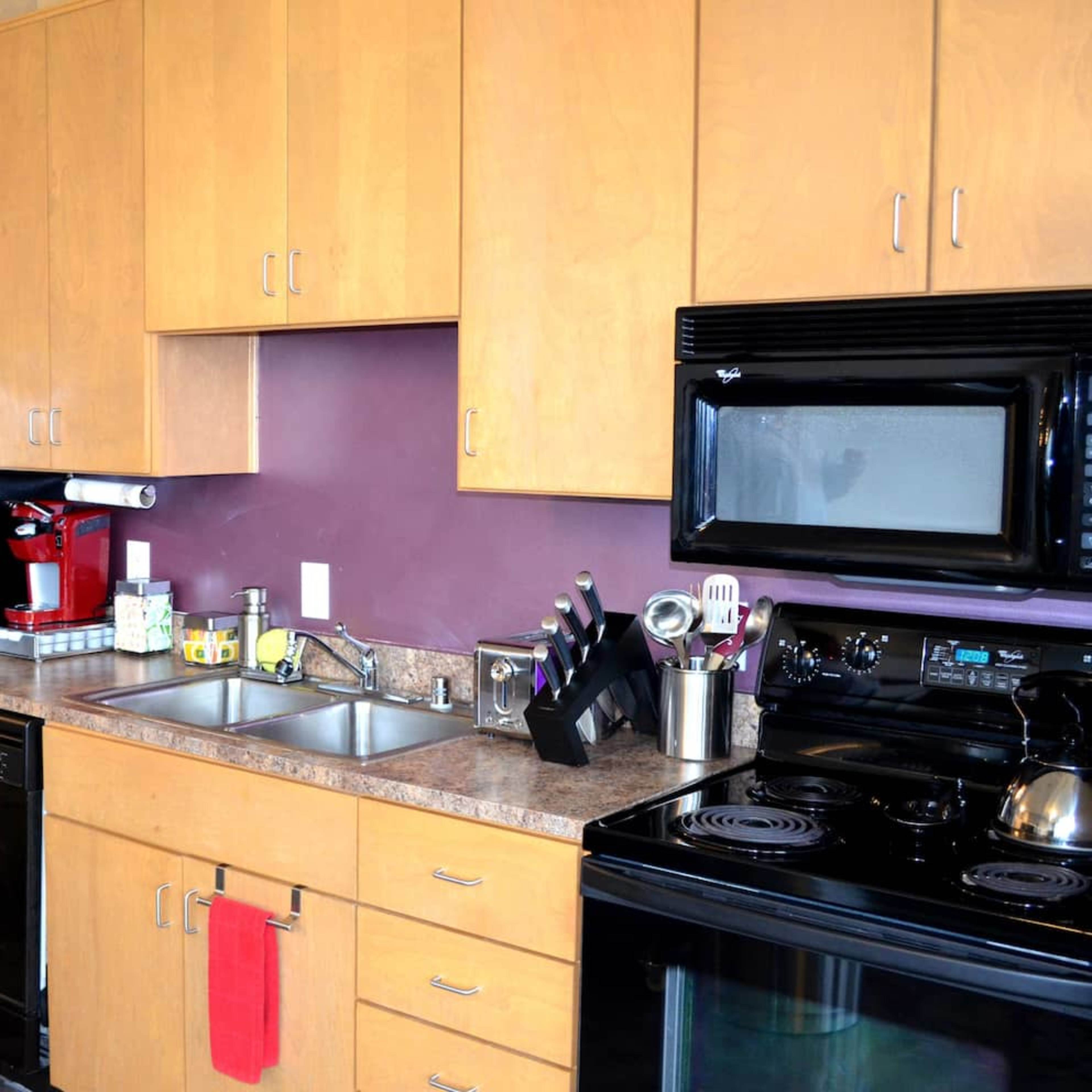 A compact kitchen with wooden cabinets, stainless steel appliances, and a black refrigerator and stove.