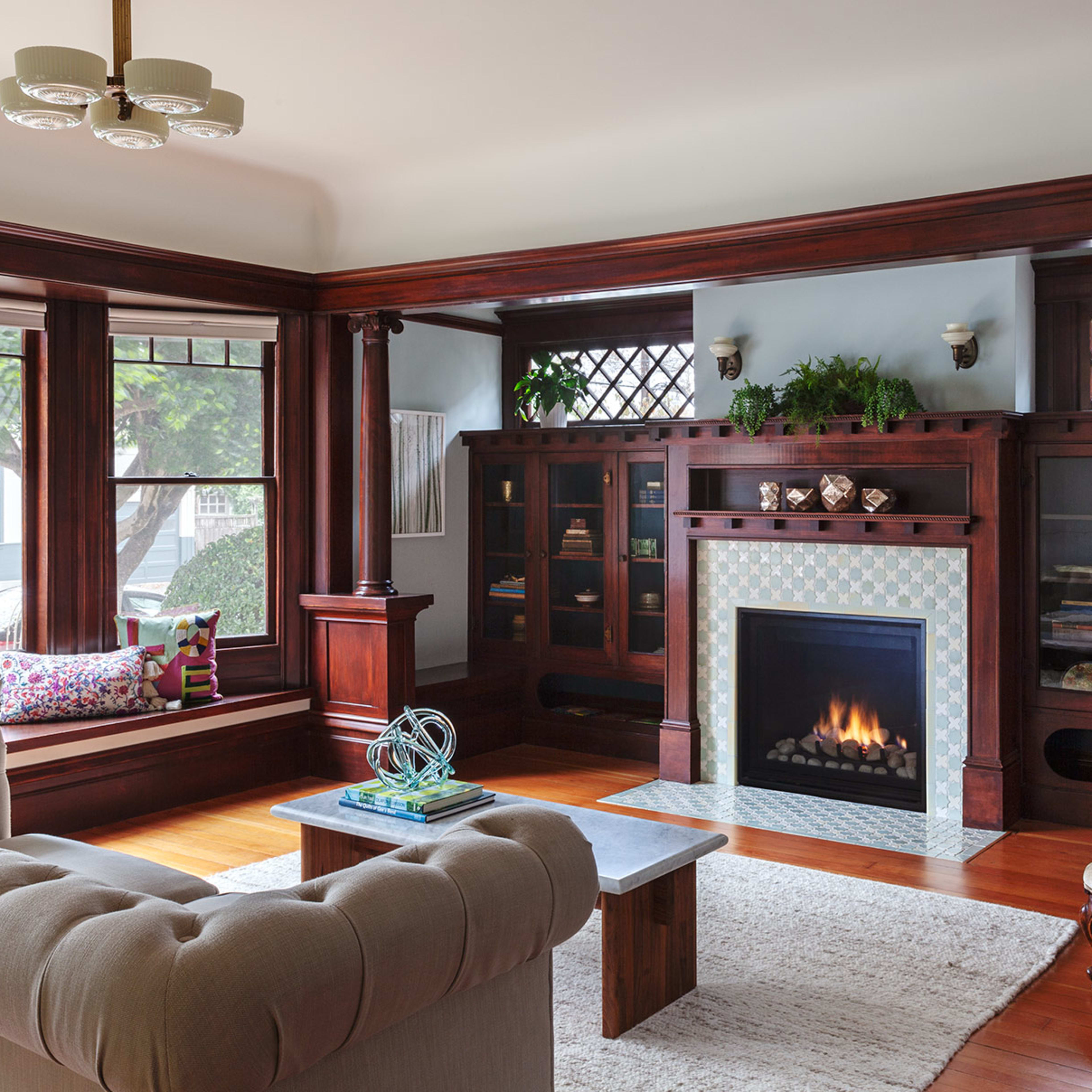 A cozy living room featuring a fireplace, wooden cabinetry, a plush sofa, and a beige armchair, with large windows allowing natural light.
