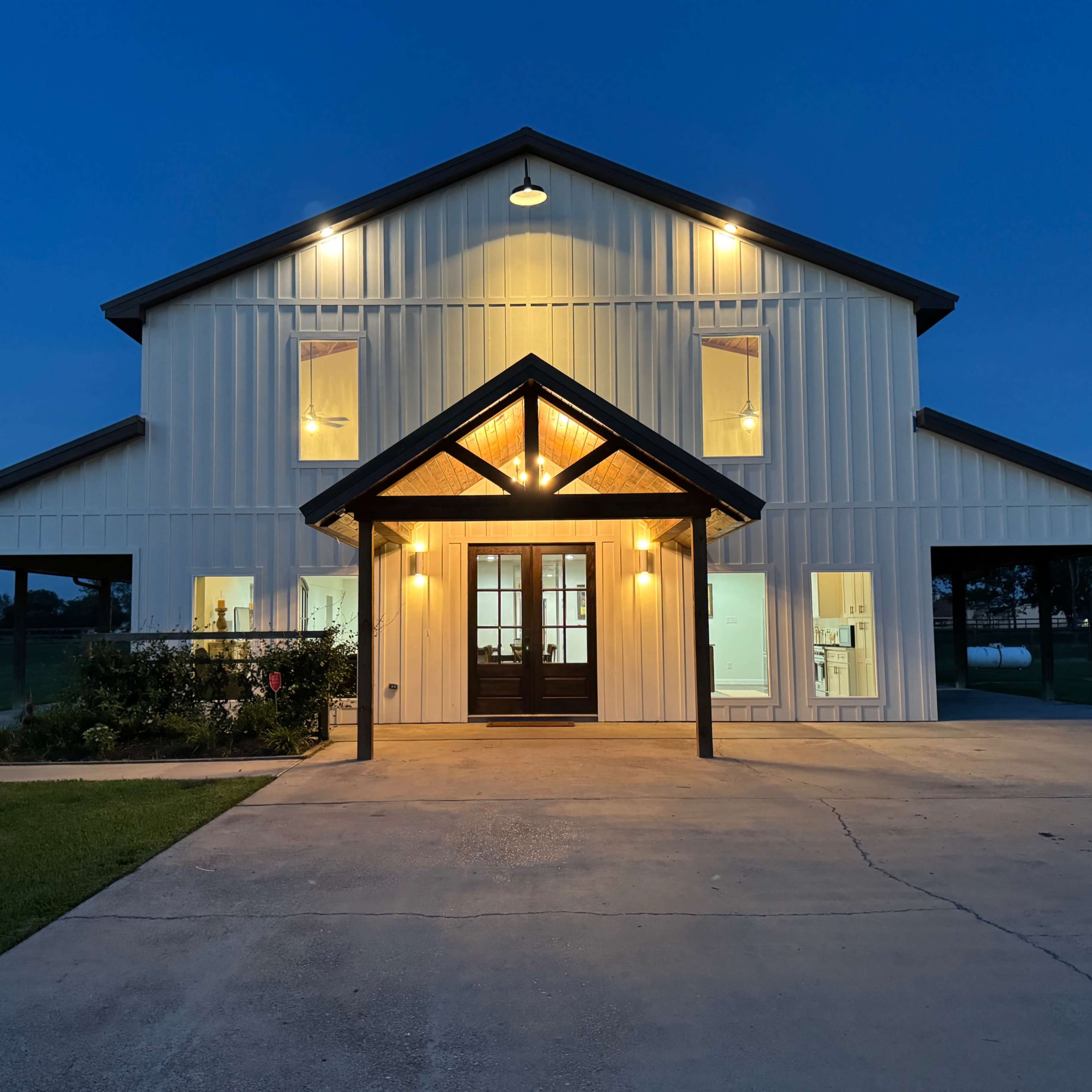 A modern farmhouse-style building is illuminated at night, featuring a gabled roof, large windows, and a front porch.