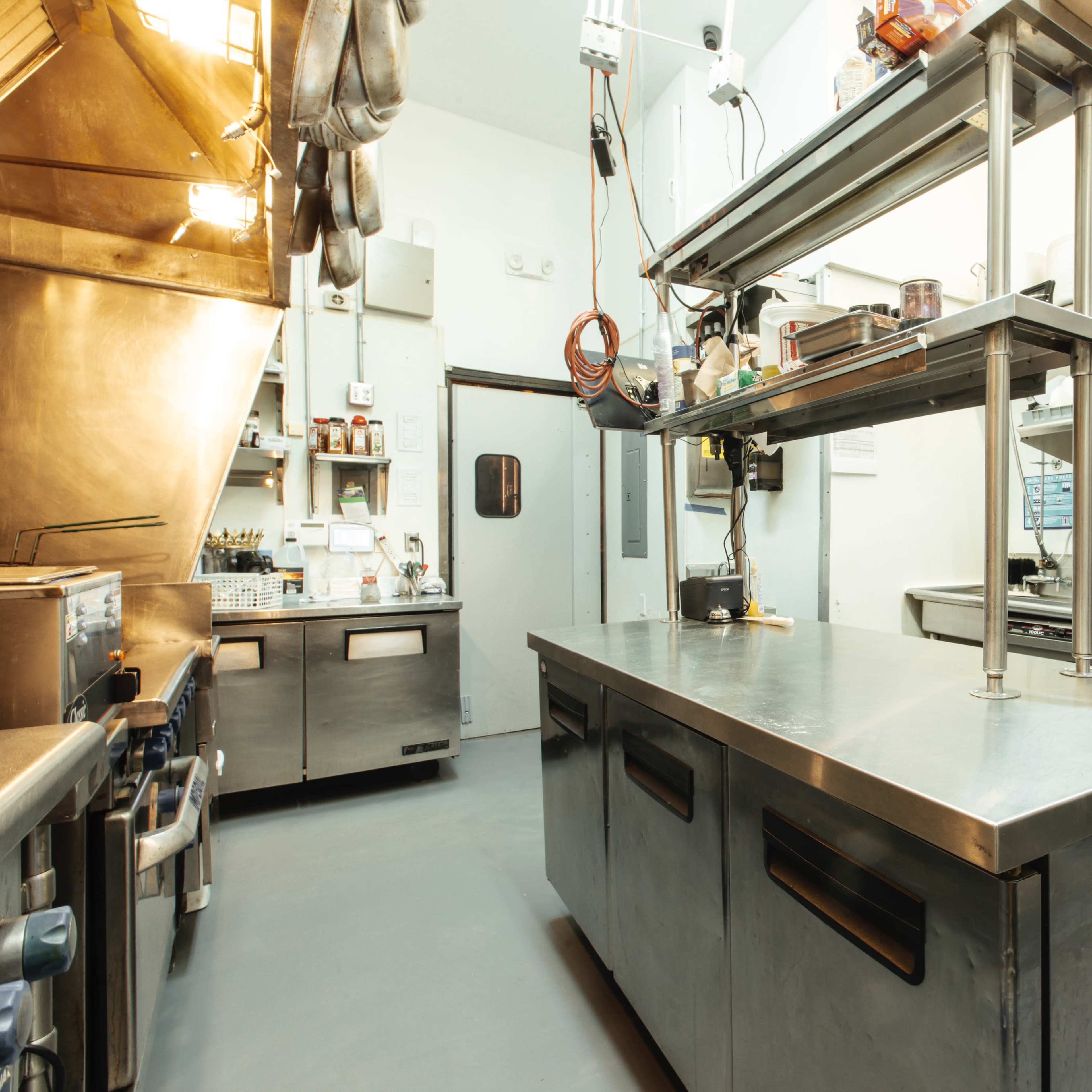 A commercial kitchen with stainless steel appliances, countertops, and shelving organized for food preparation.