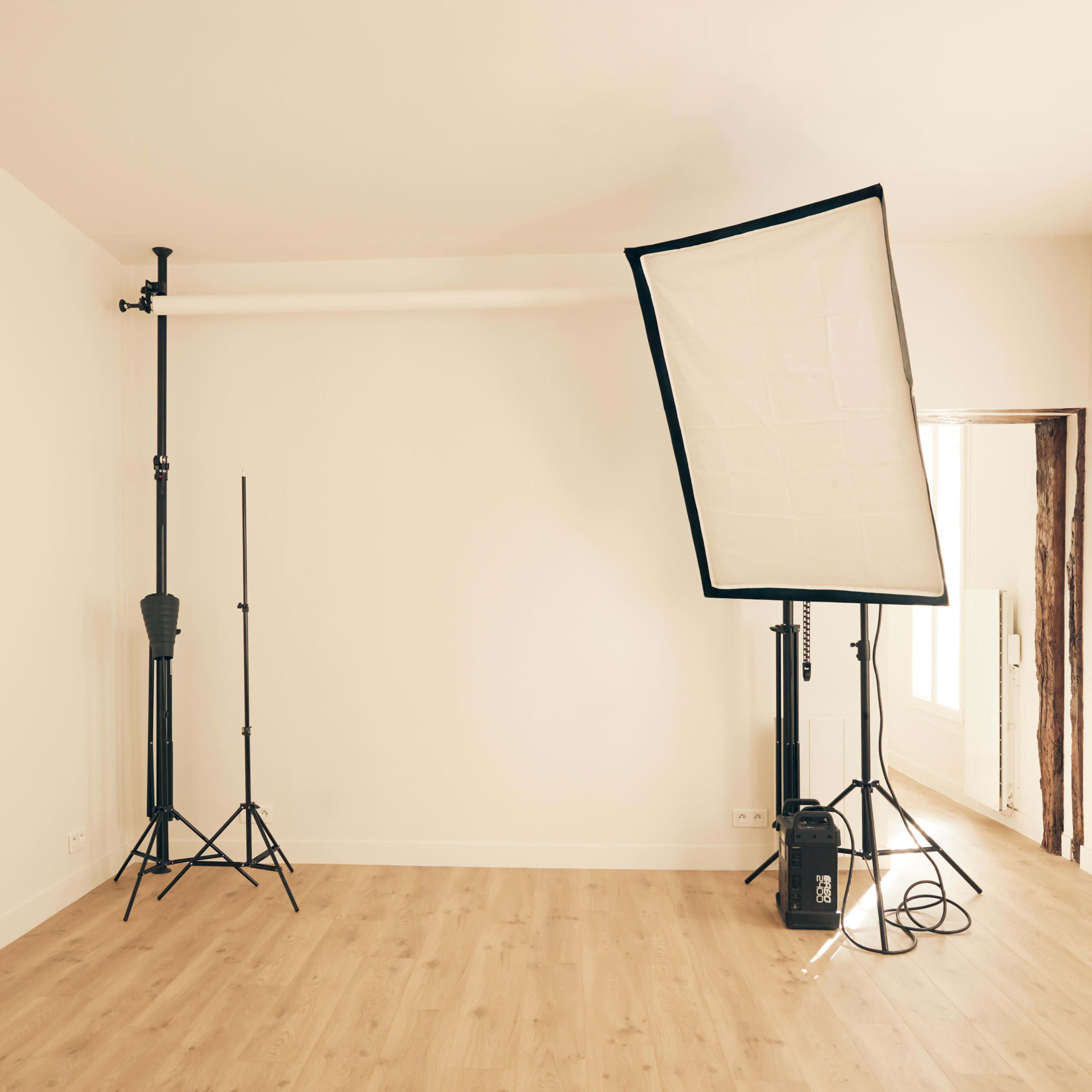 A minimalistic studio space featuring two light stands and a large softbox against a plain wall.