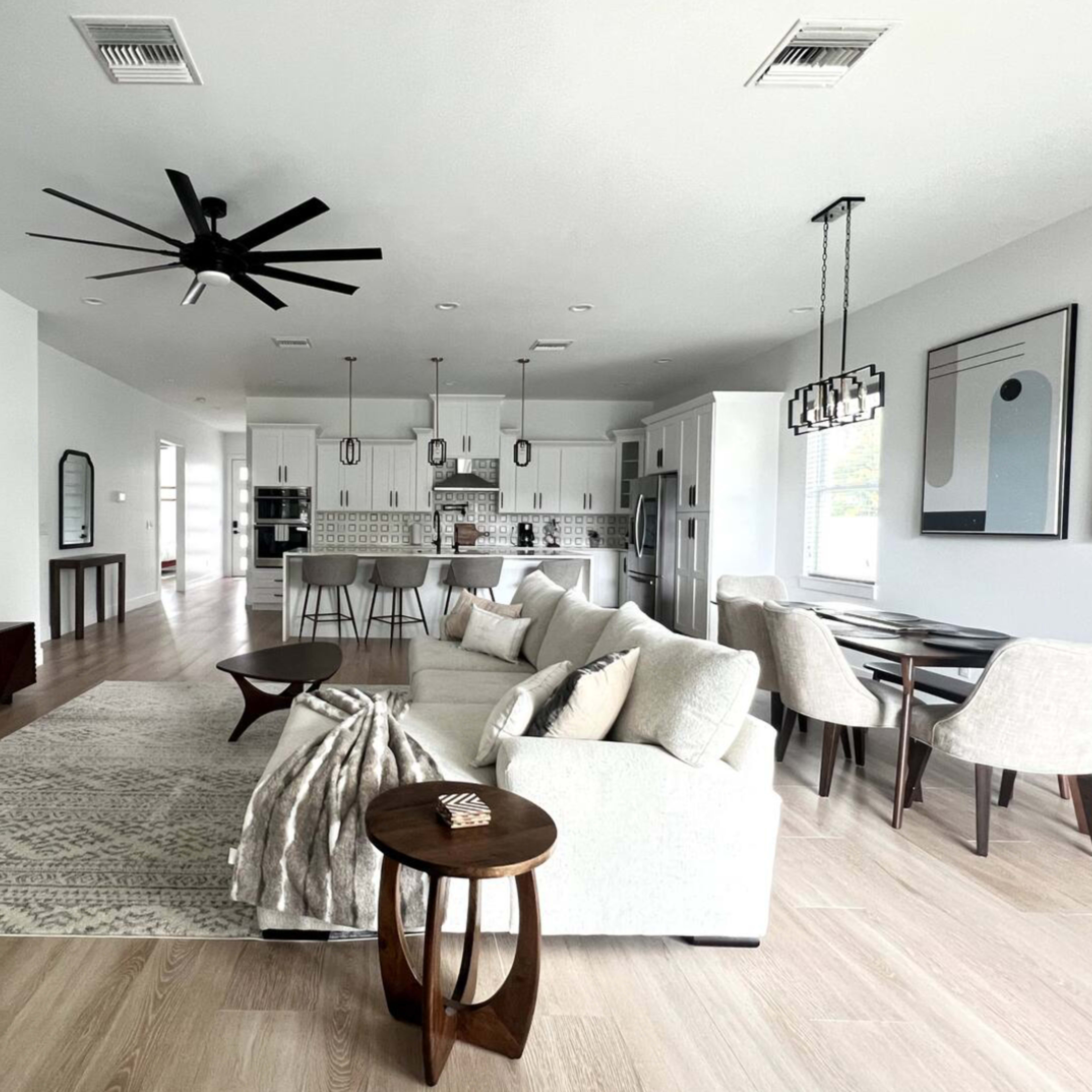A modern, open-concept living space with a white sofa, a light area rug, a dining table, and a kitchen in the background.