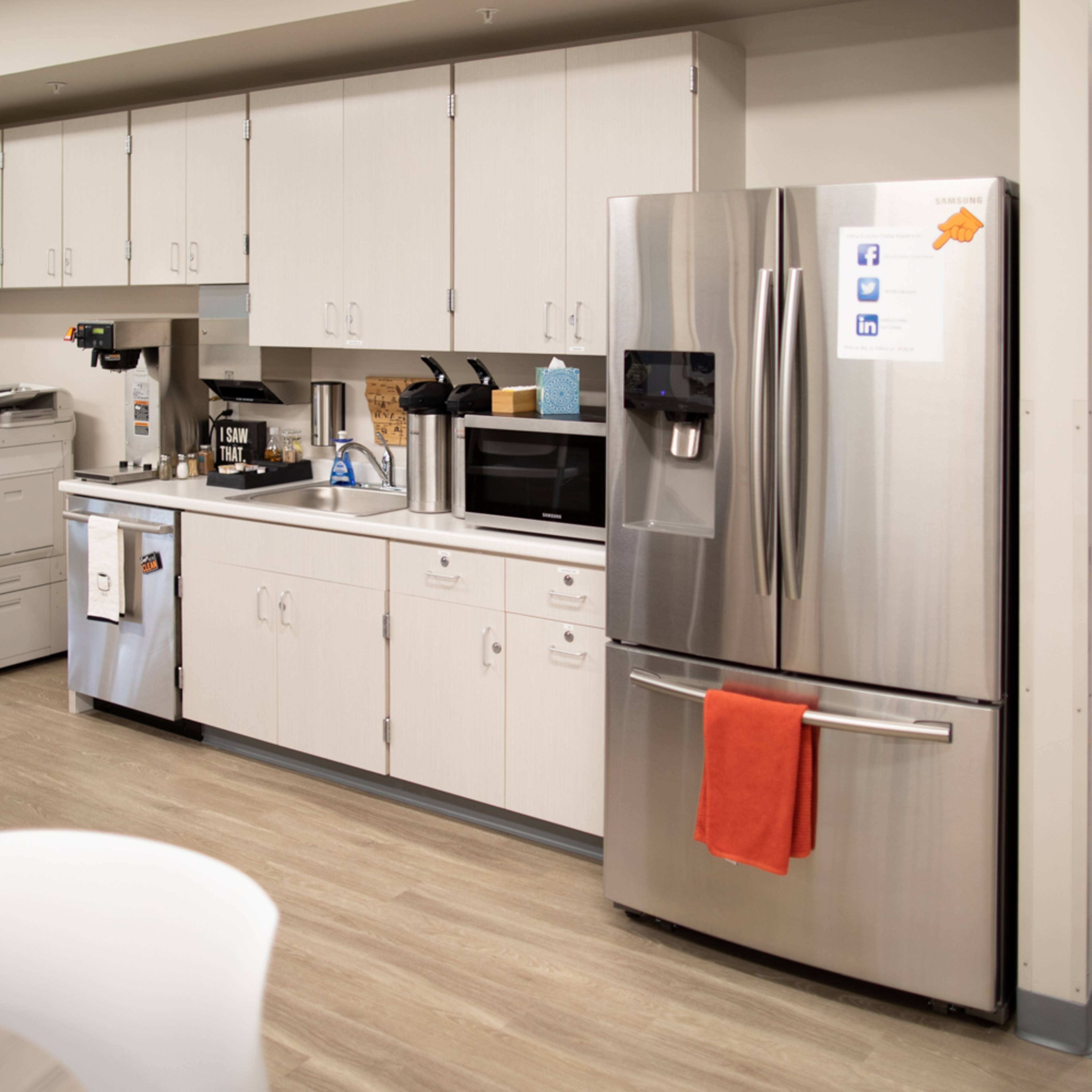 A modern kitchen area with cabinetry, a refrigerator, a microwave, and coffee-making equipment.