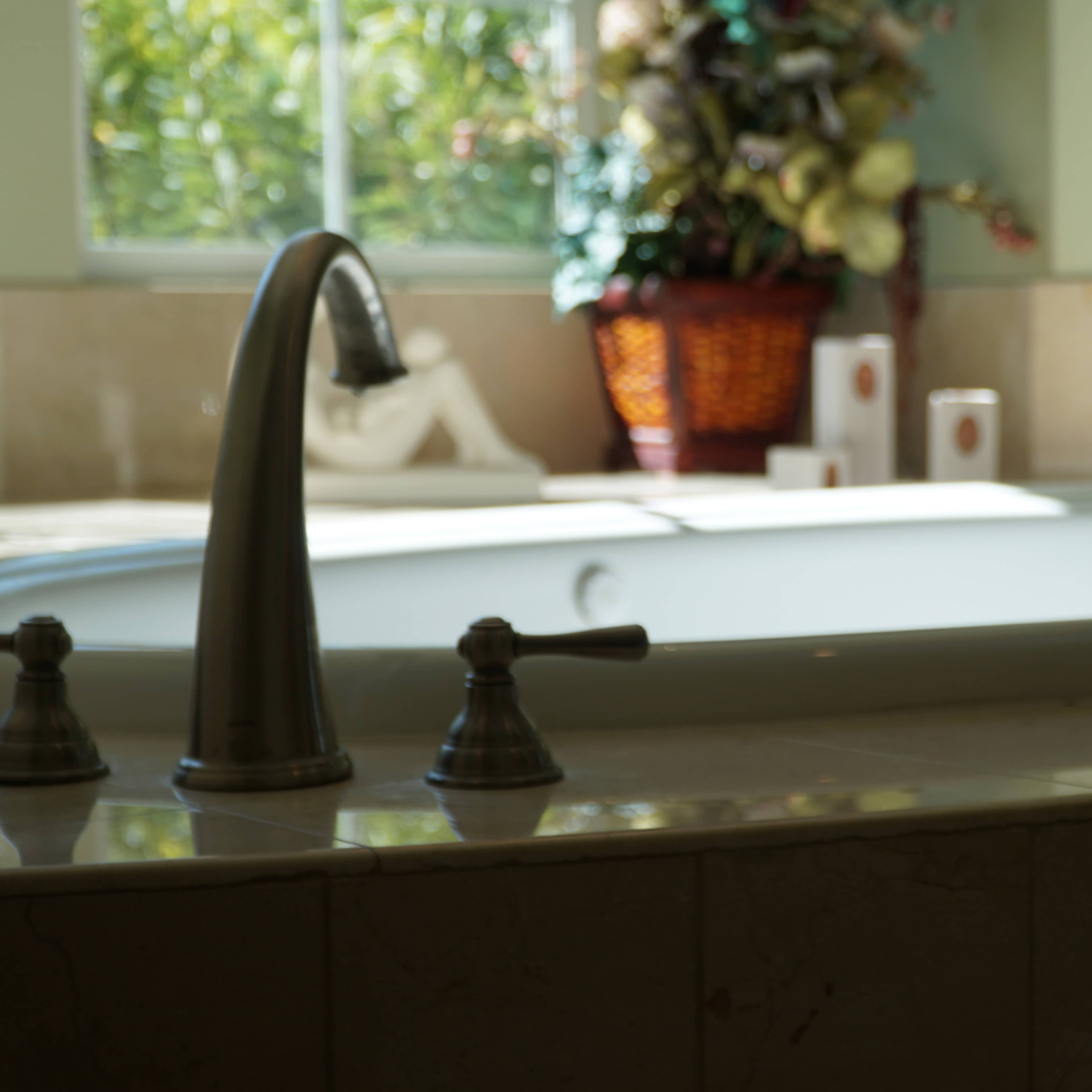 A bathroom with a large, white bathtub surrounded by light-colored tiles and a window letting in natural light.
