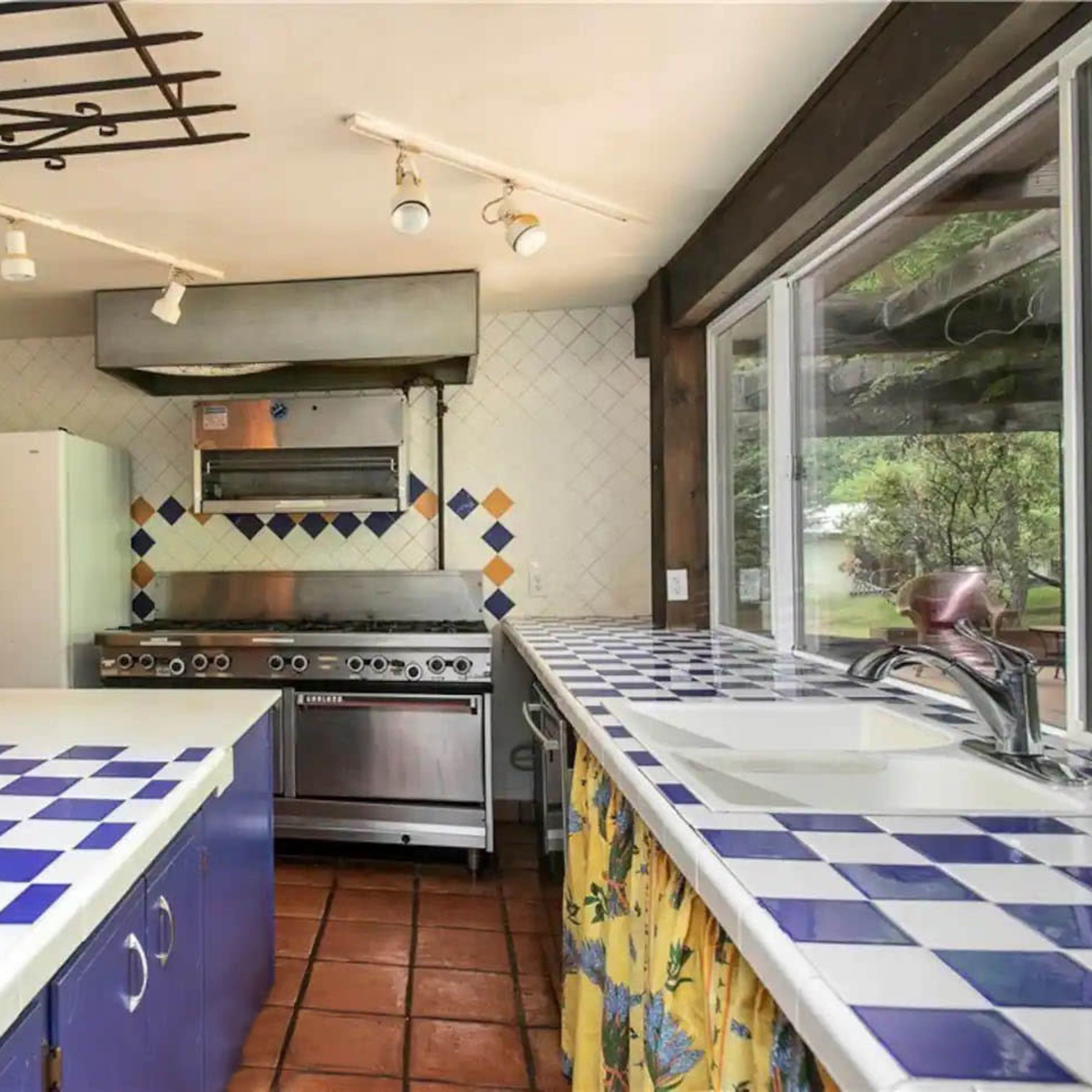 A kitchen with blue and white checkered countertops, a stainless steel stove, and a white refrigerator against tiled walls.