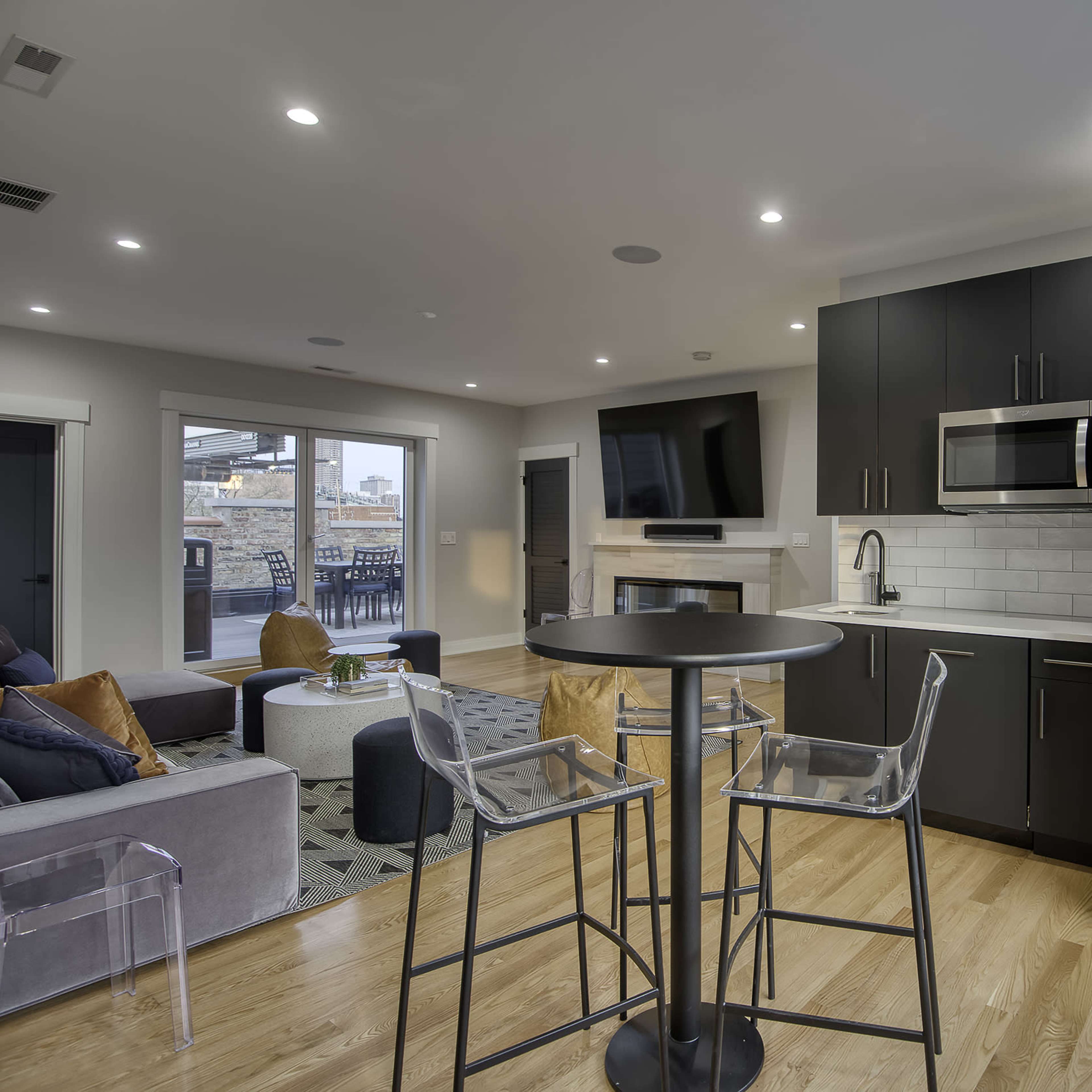 A modern kitchen and living area are shown with sleek black cabinetry, stainless steel appliances, and a cozy seating arrangement.