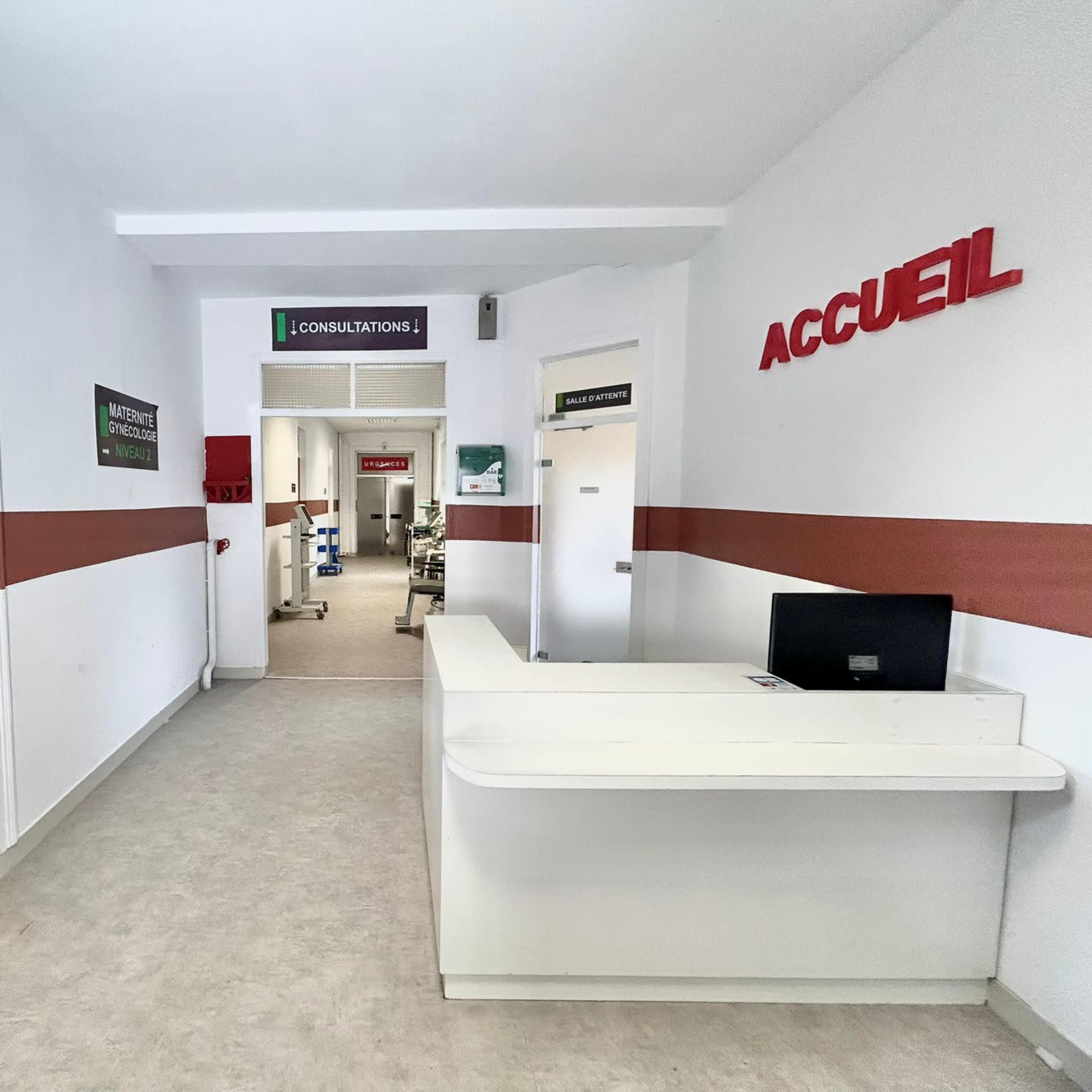 A well-lit hospital corridor featuring a reception desk and signs indicating consultations and patient reception areas.