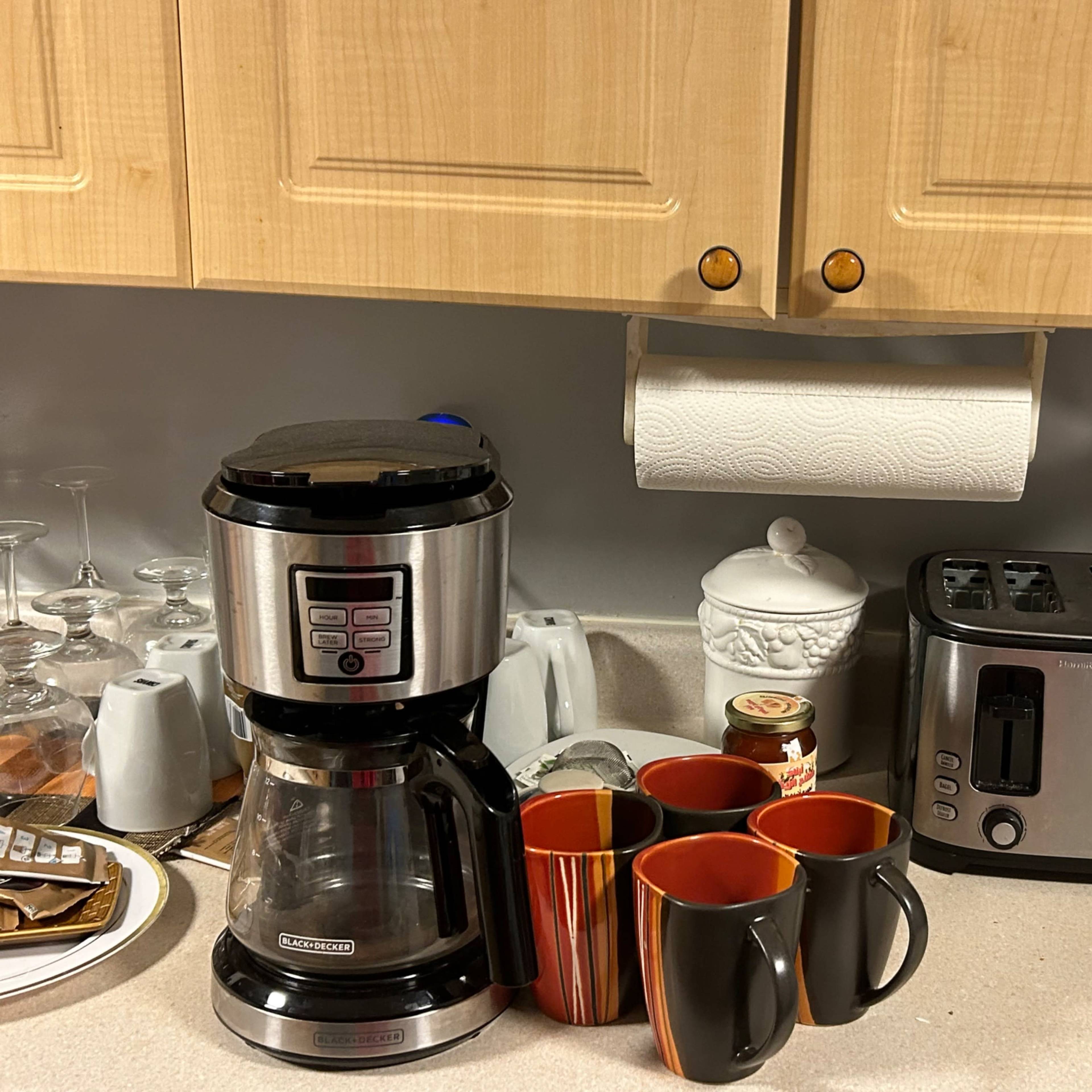 A coffee maker and a toaster are positioned on a kitchen counter alongside several mugs and a paper towel holder.