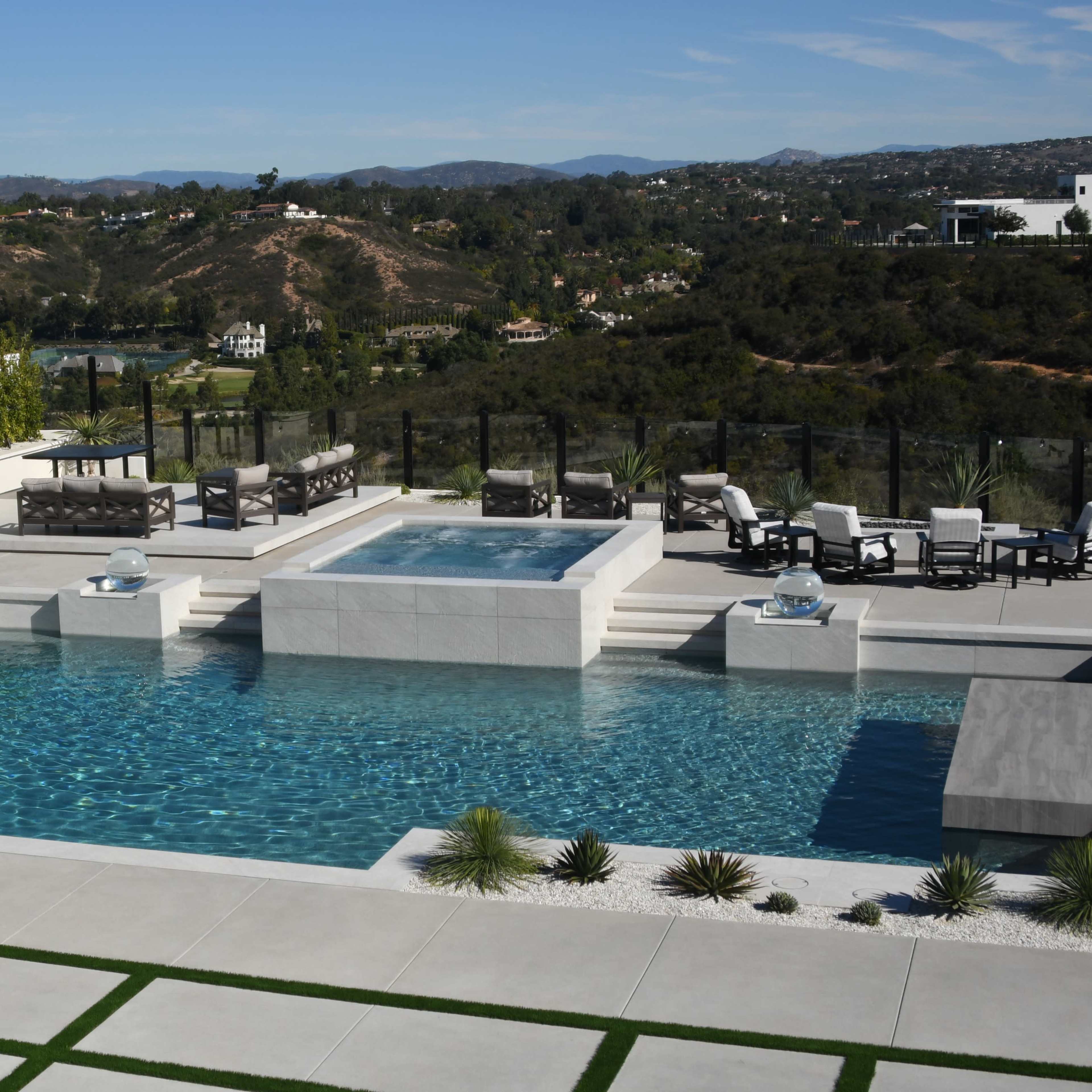 A modern outdoor space featuring a swimming pool, hot tub, and multiple seating areas overlooking a hilly landscape.