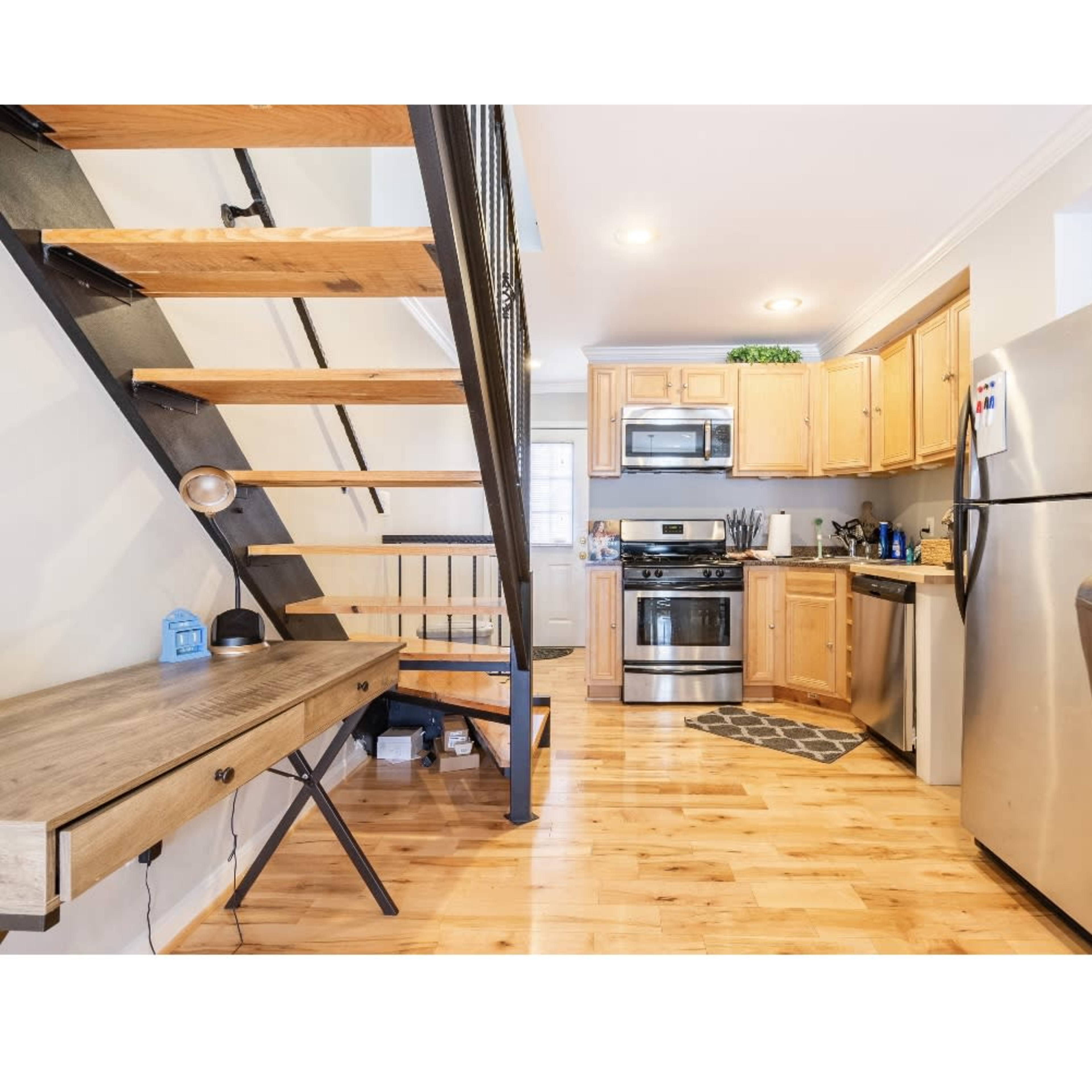 A compact kitchen area with wooden cabinets, stainless steel appliances, and a staircase leading to an upper level.