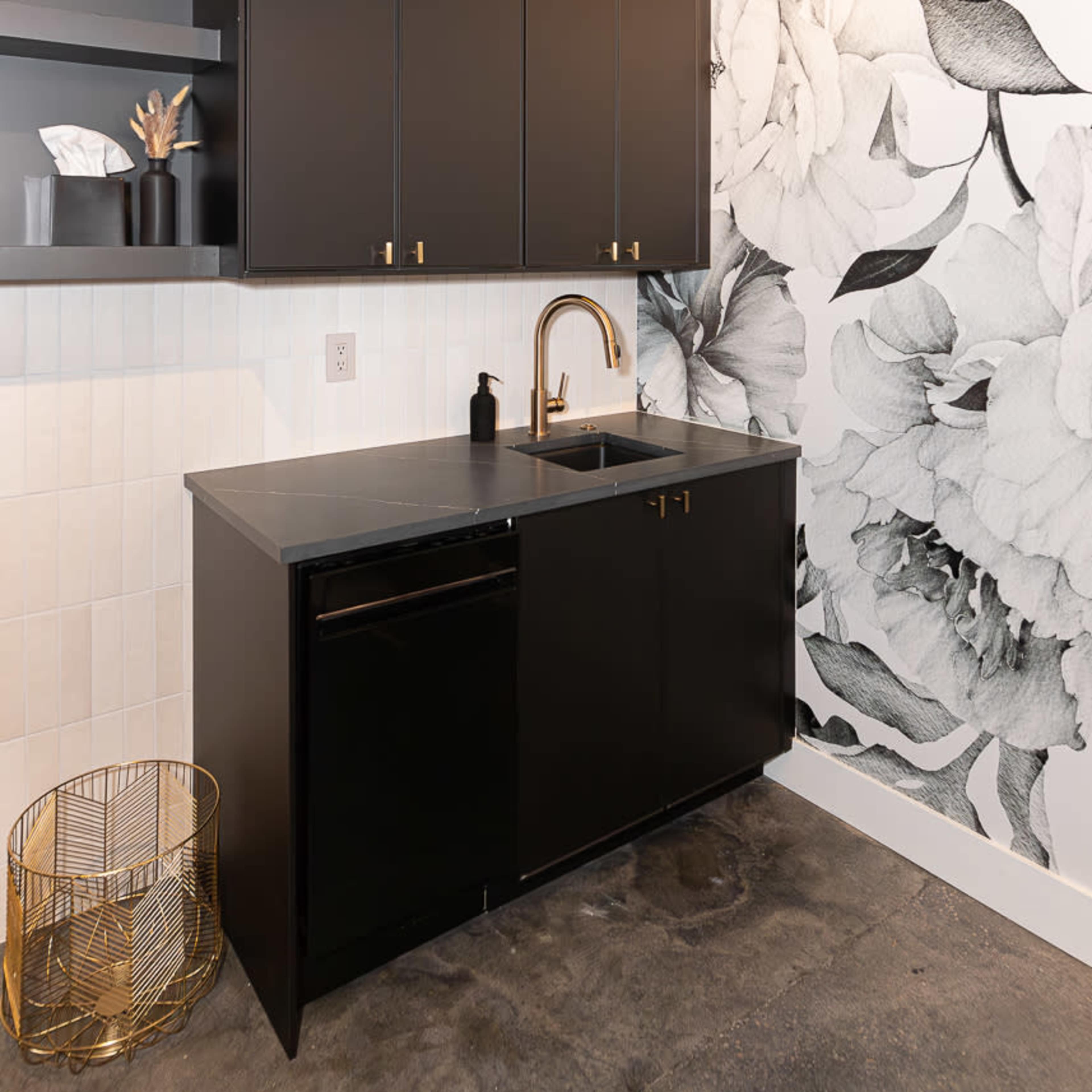 A modern kitchen with black cabinetry, a stainless steel sink, and a large floral wallpaper mural on one wall.