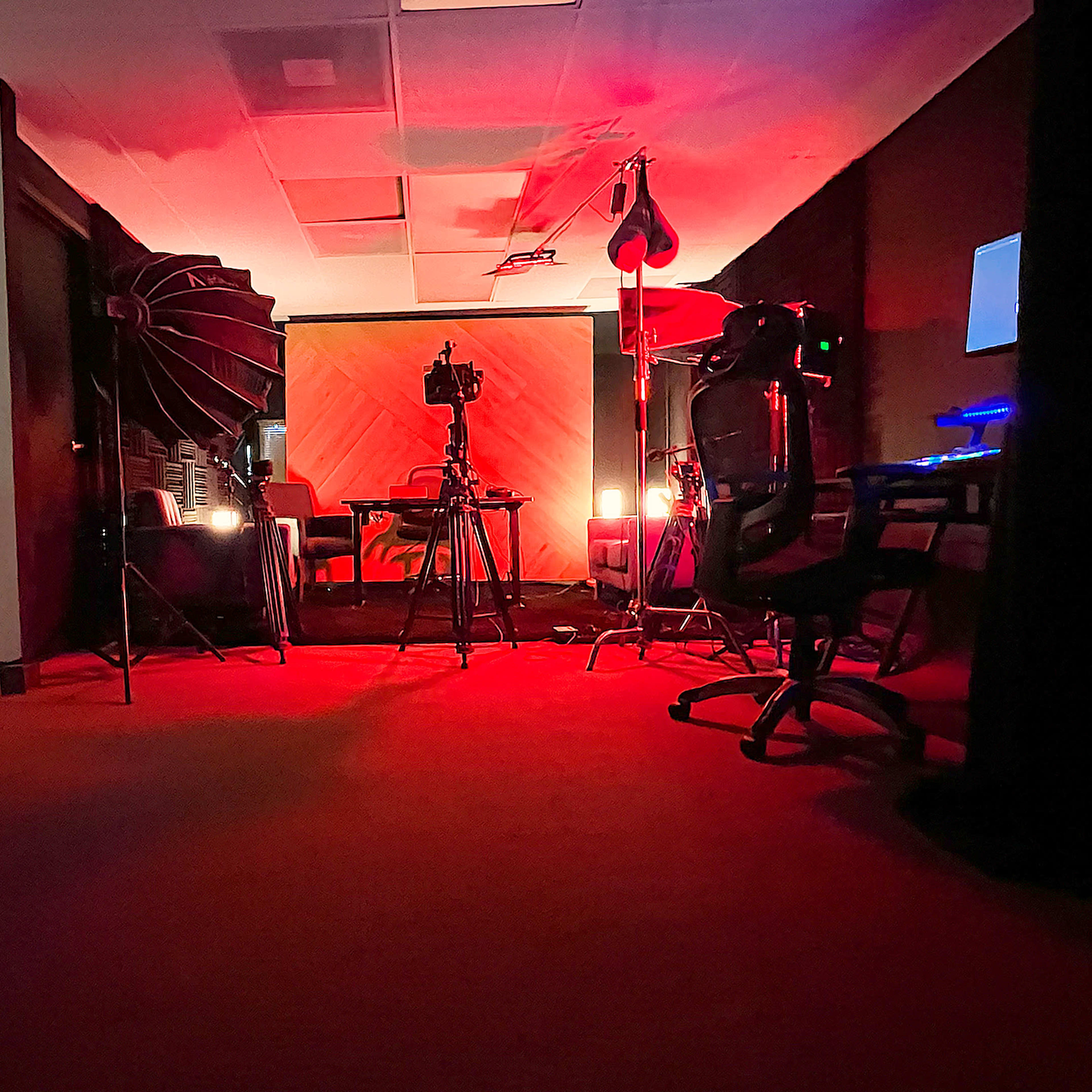 A dimly lit studio setting featuring a backdrop, lighting equipment, and various audio-visual gear.