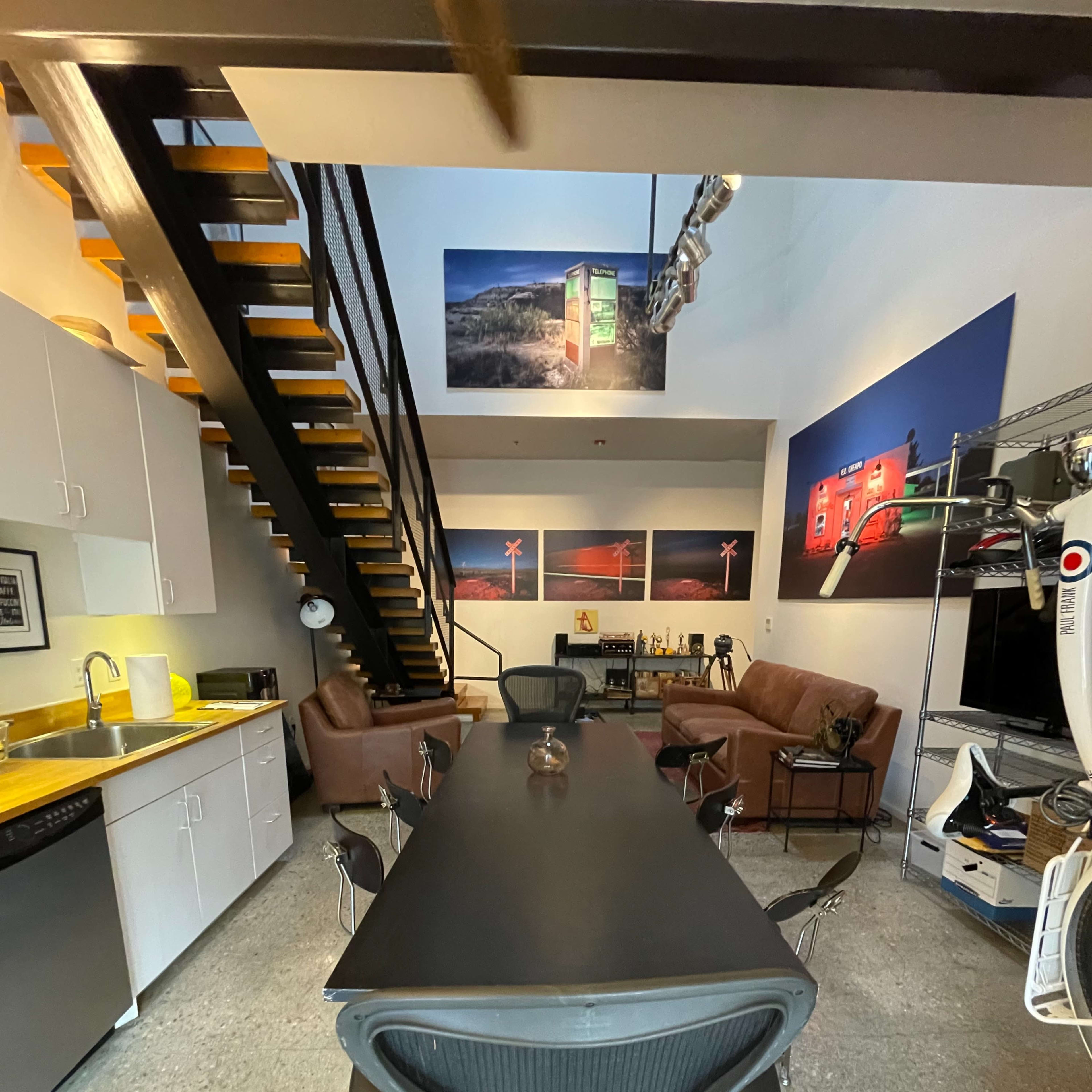 A modern office space with a long black conference table, several chairs, a staircase, and large photographs on the walls.