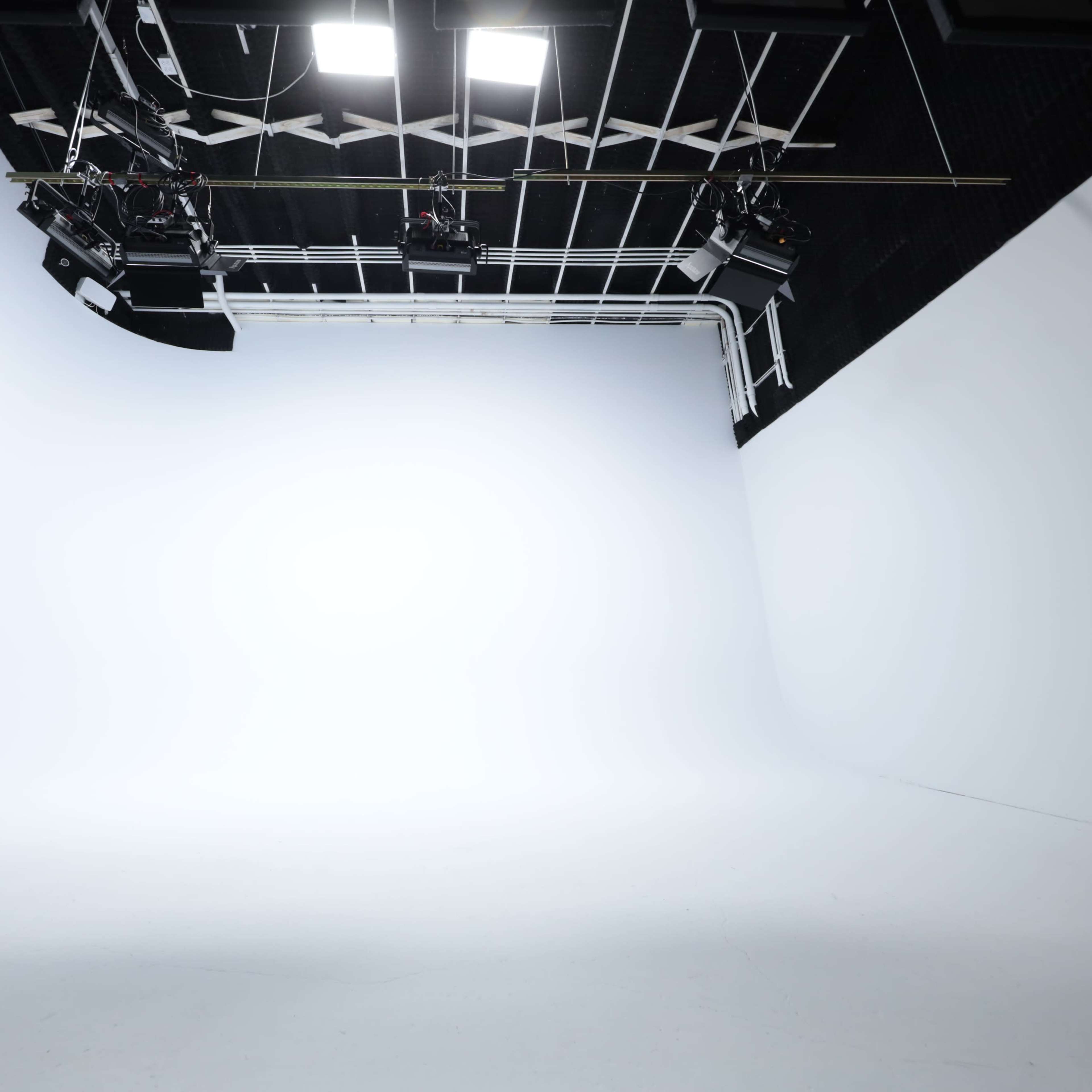A large, empty photography studio with seamless white backdrops and overhead lighting equipment.
