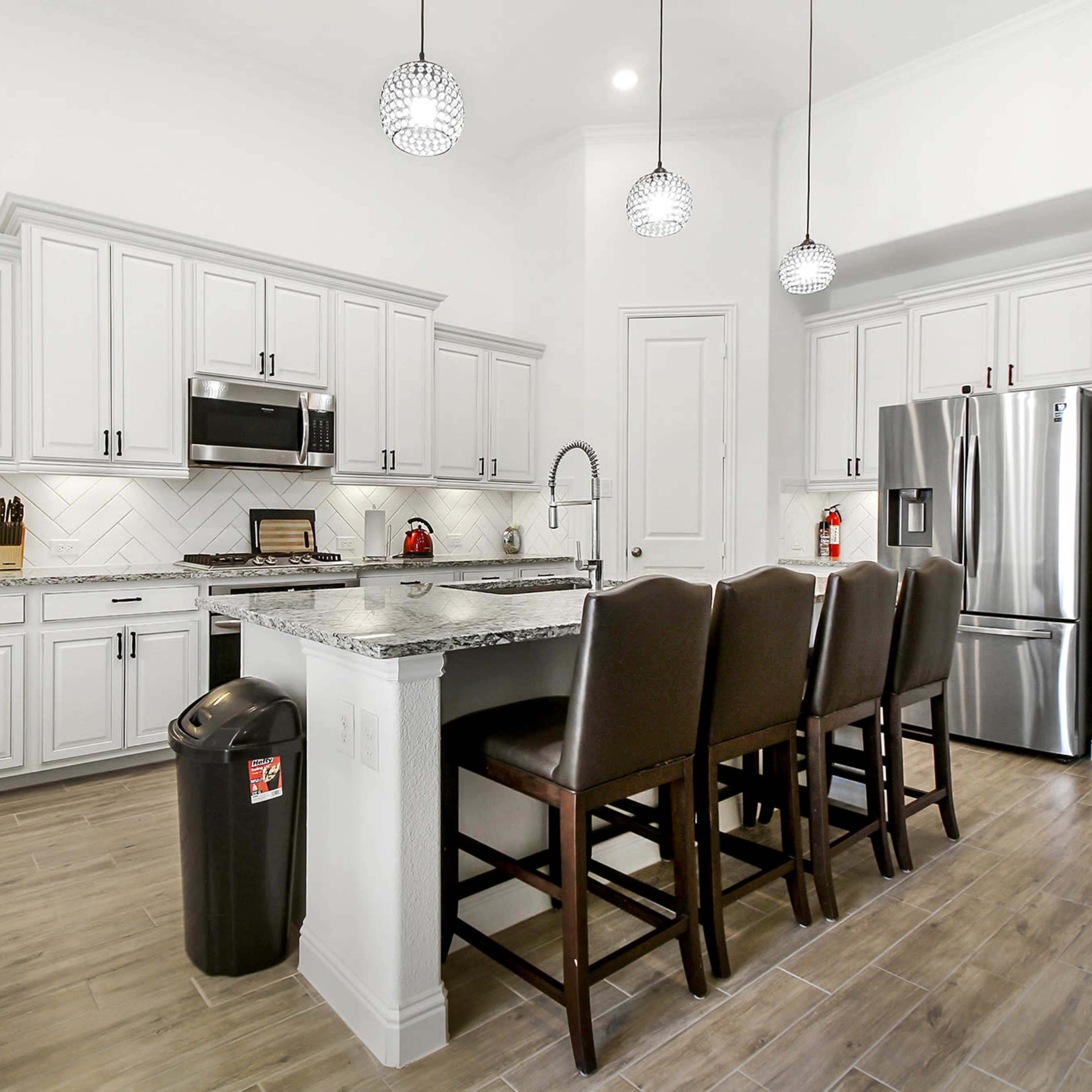 The kitchen features white cabinetry, a gray granite island with seating for four, stainless steel appliances, and a tiled backsplash.