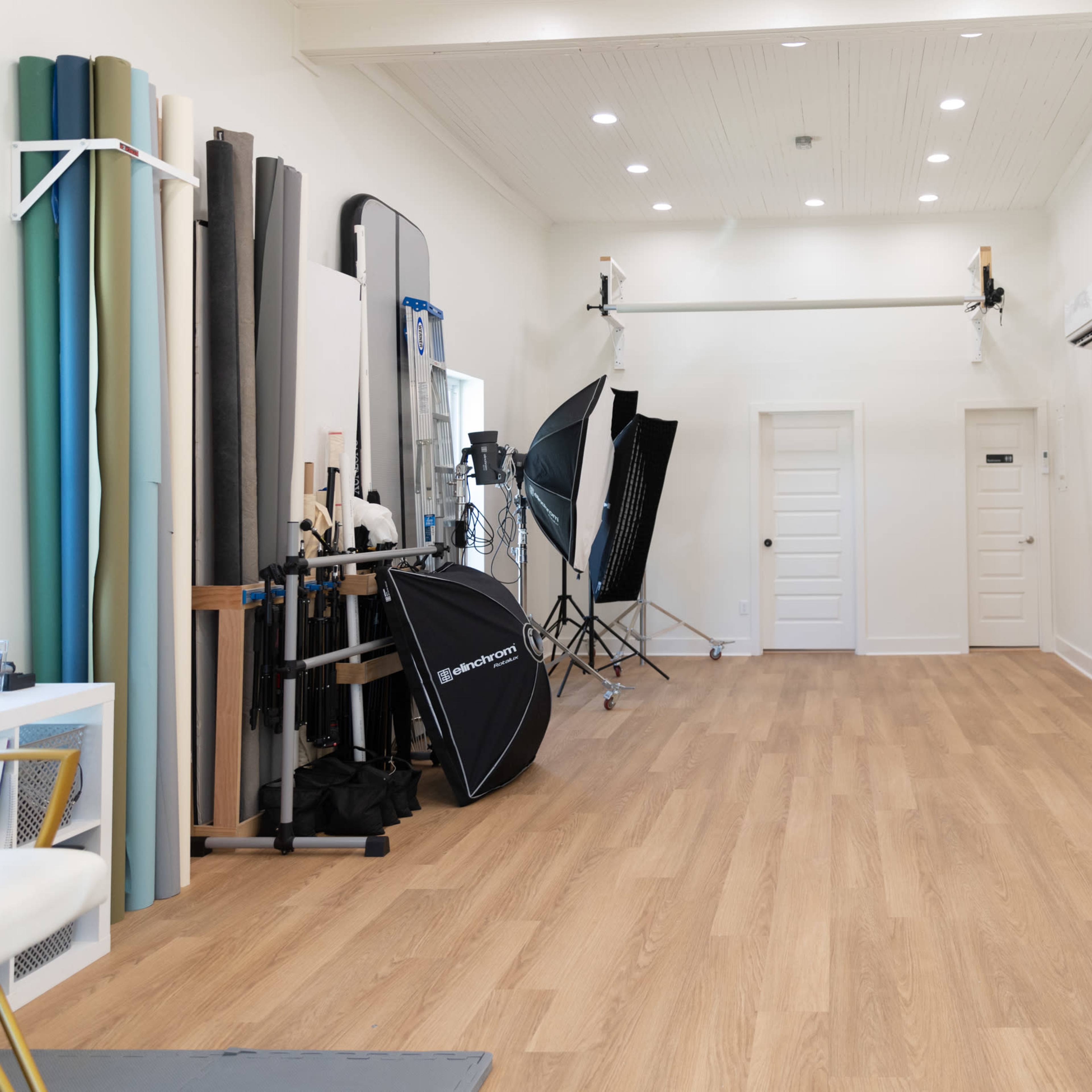 A spacious photography studio with various backdrops, lighting equipment, and a door at one end.