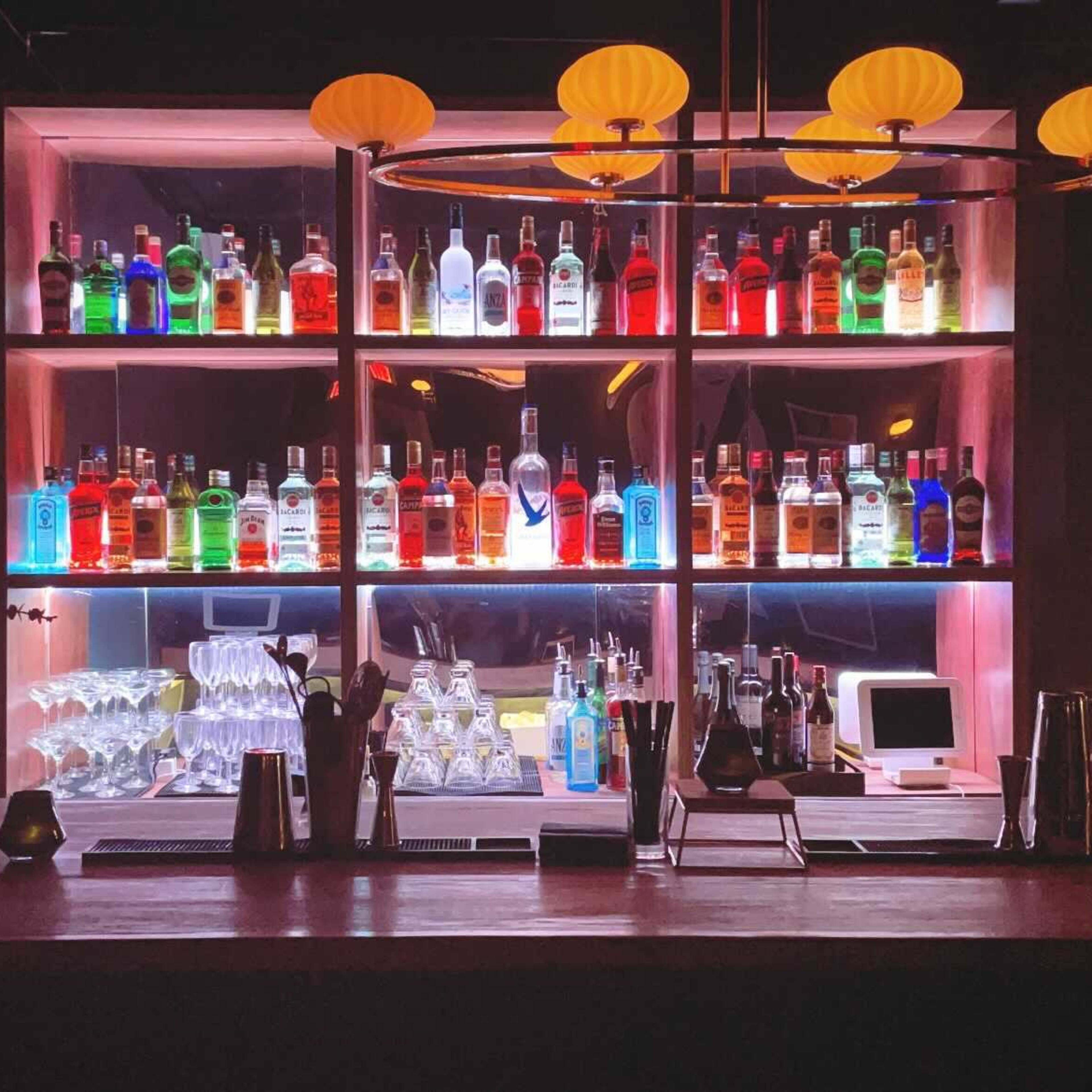 A well-lit bar displays an assortment of colorful liquor bottles arranged on shelves behind a sleek counter.