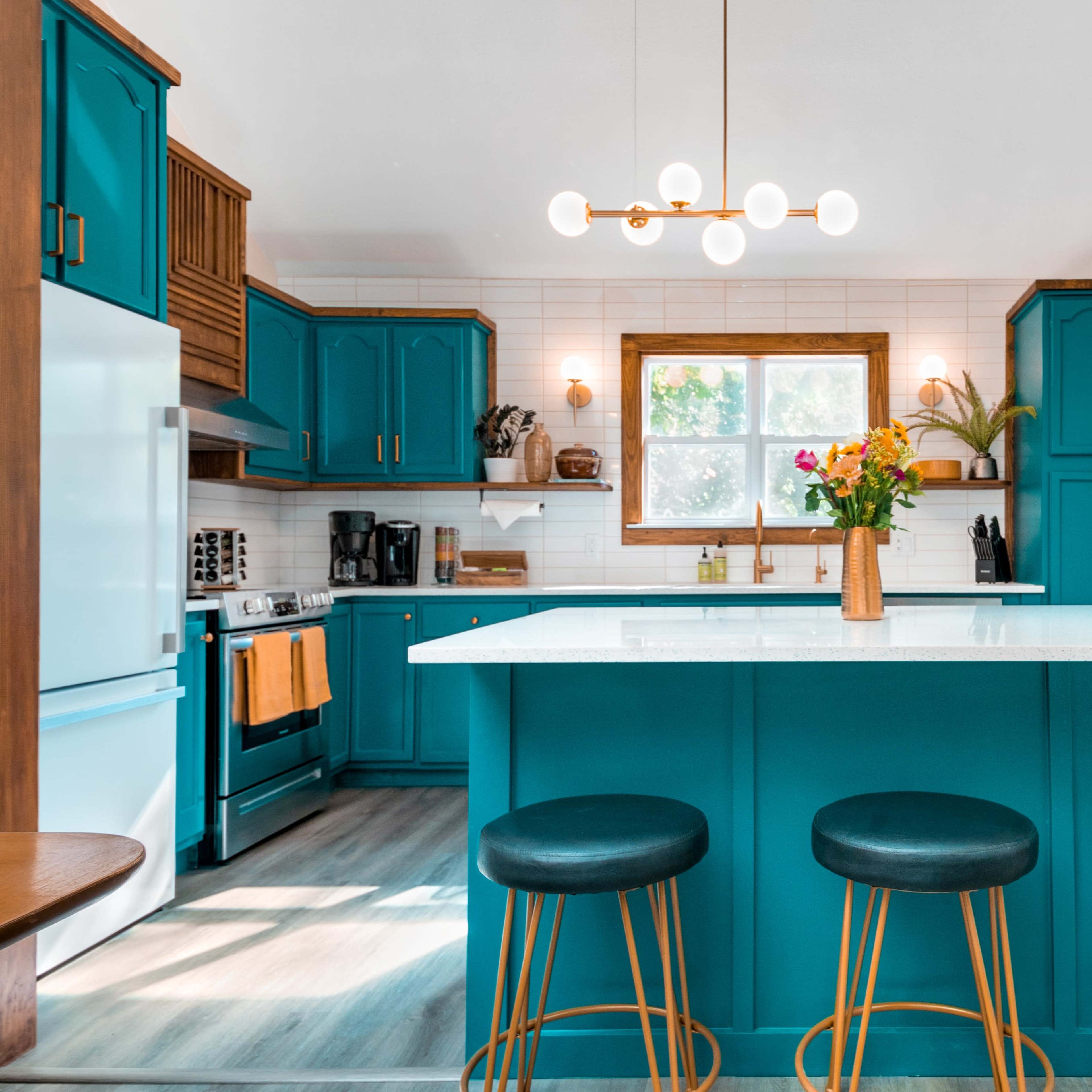 A modern kitchen featuring teal cabinetry, a central island with seating, and a large window providing natural light.