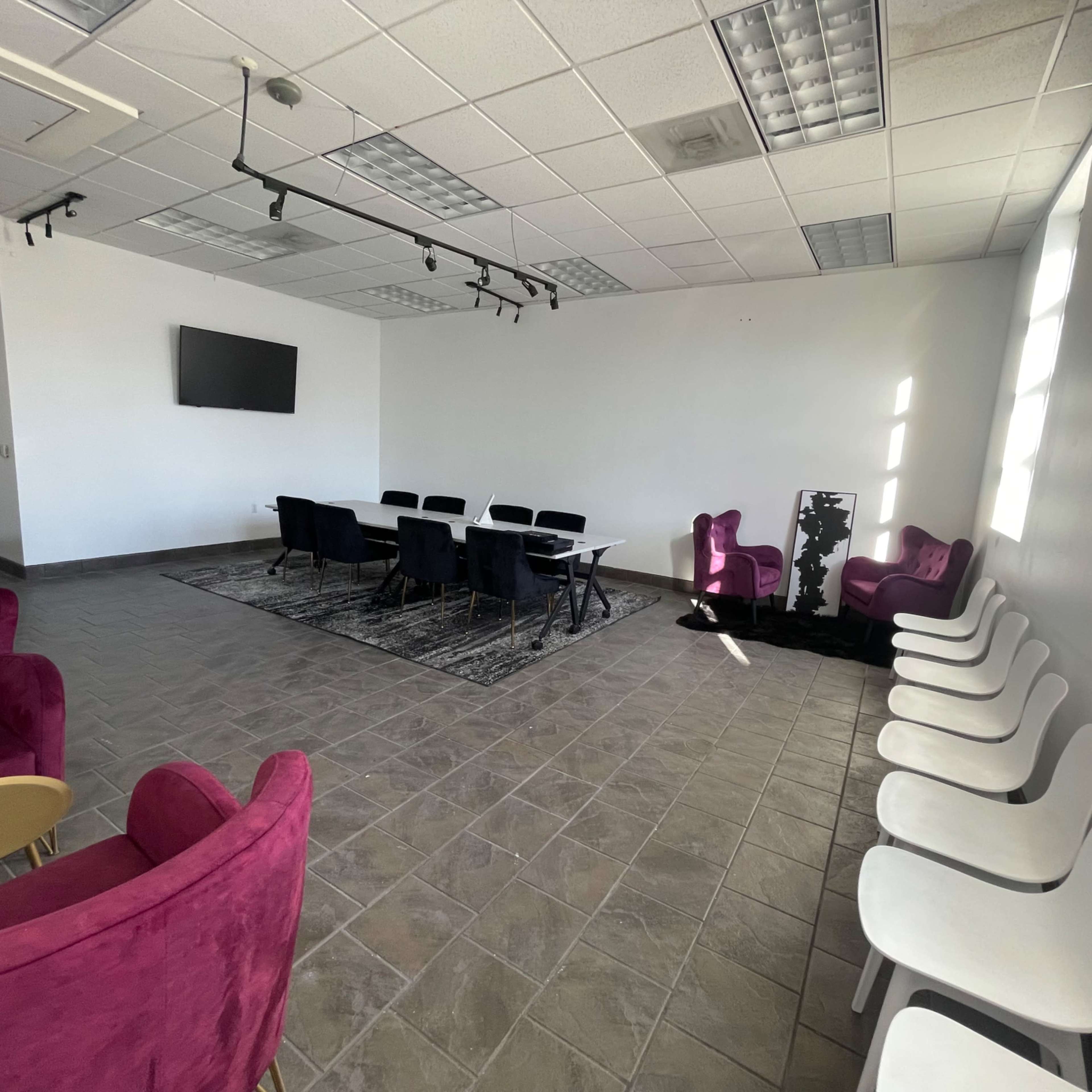 A modern meeting room with a table and chairs centered in the space, surrounded by purple and white seating along the walls.