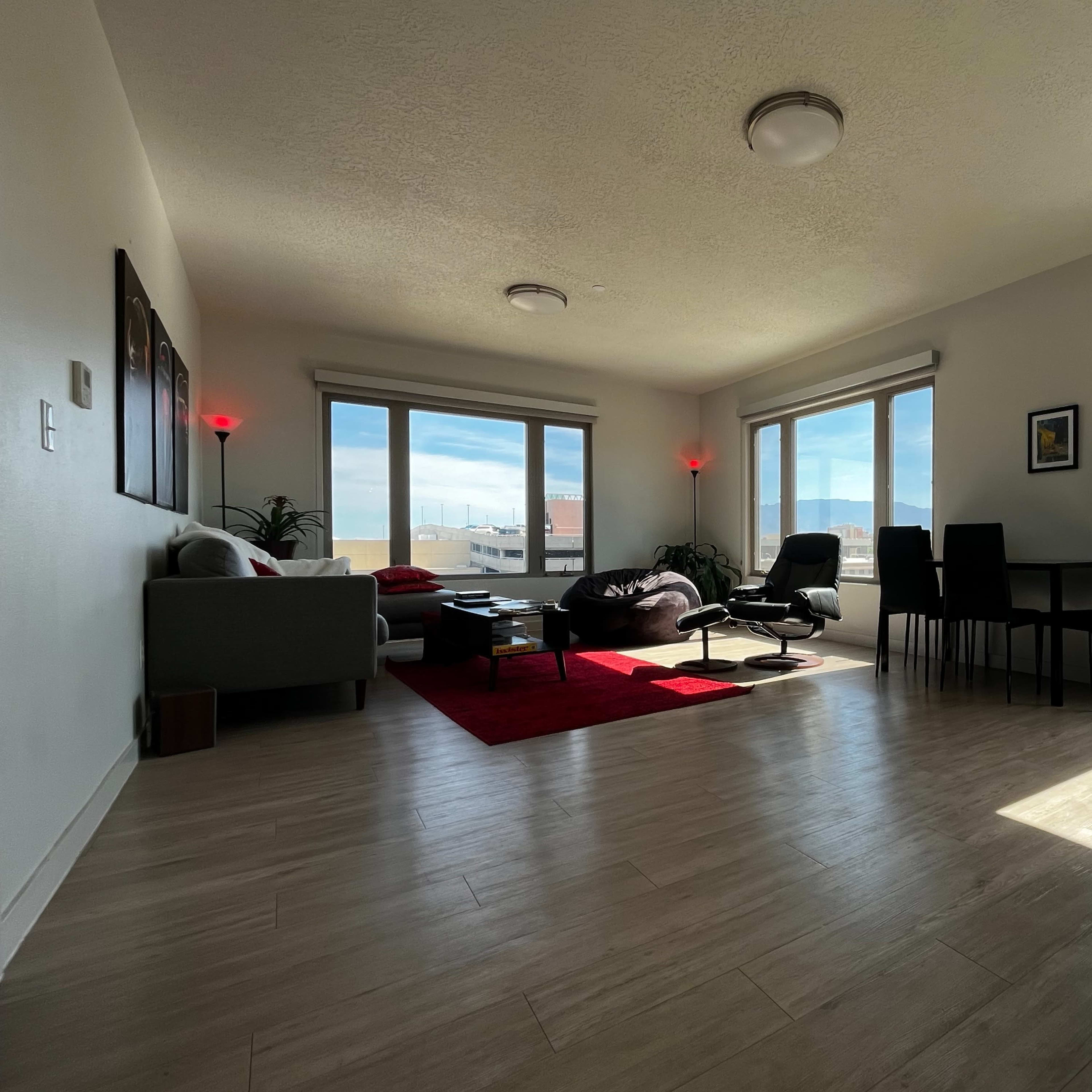 A bright living room with large windows, a sofa, a coffee table, and a dining area, all set against a view of distant mountains.